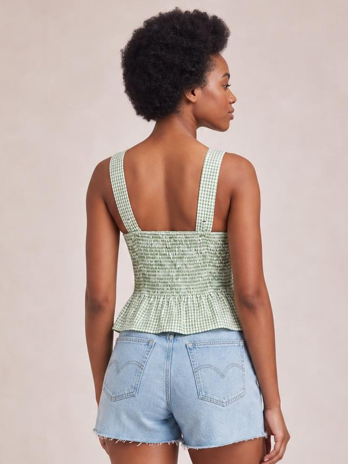 Model shown from behind looking over her shoulder in a green plaid smocked tank with wide straps, a fitted bodice, and a softly flared hem.