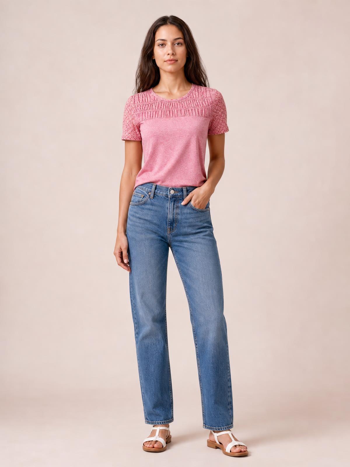 A model wears a pink smocked round-neck short-sleeve T-shirt with textured cutout details across the yoke and sleeves, styled in a fitted silhouette.