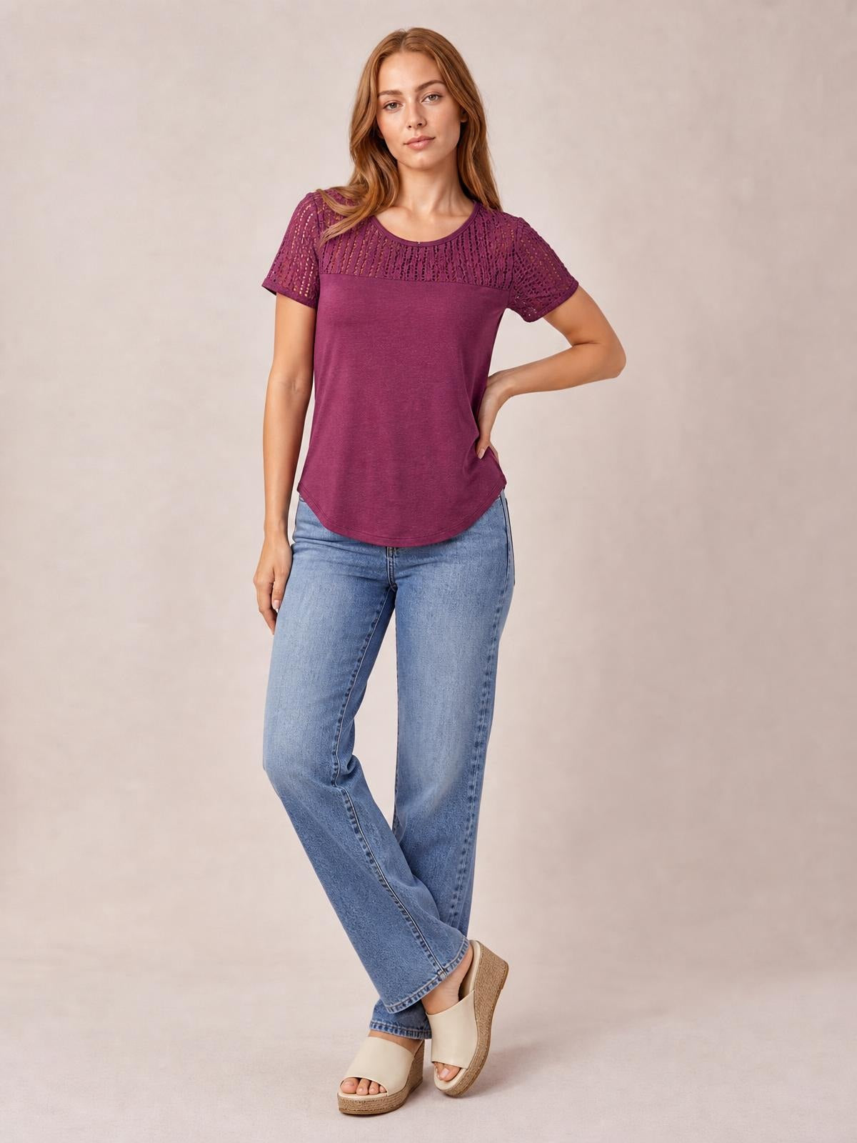 Model wearing a burgundy smocked round-neck short-sleeve T-shirt with semi-sheer cutout detailing, relaxed silhouette, curved hem, and one hand on her hip.