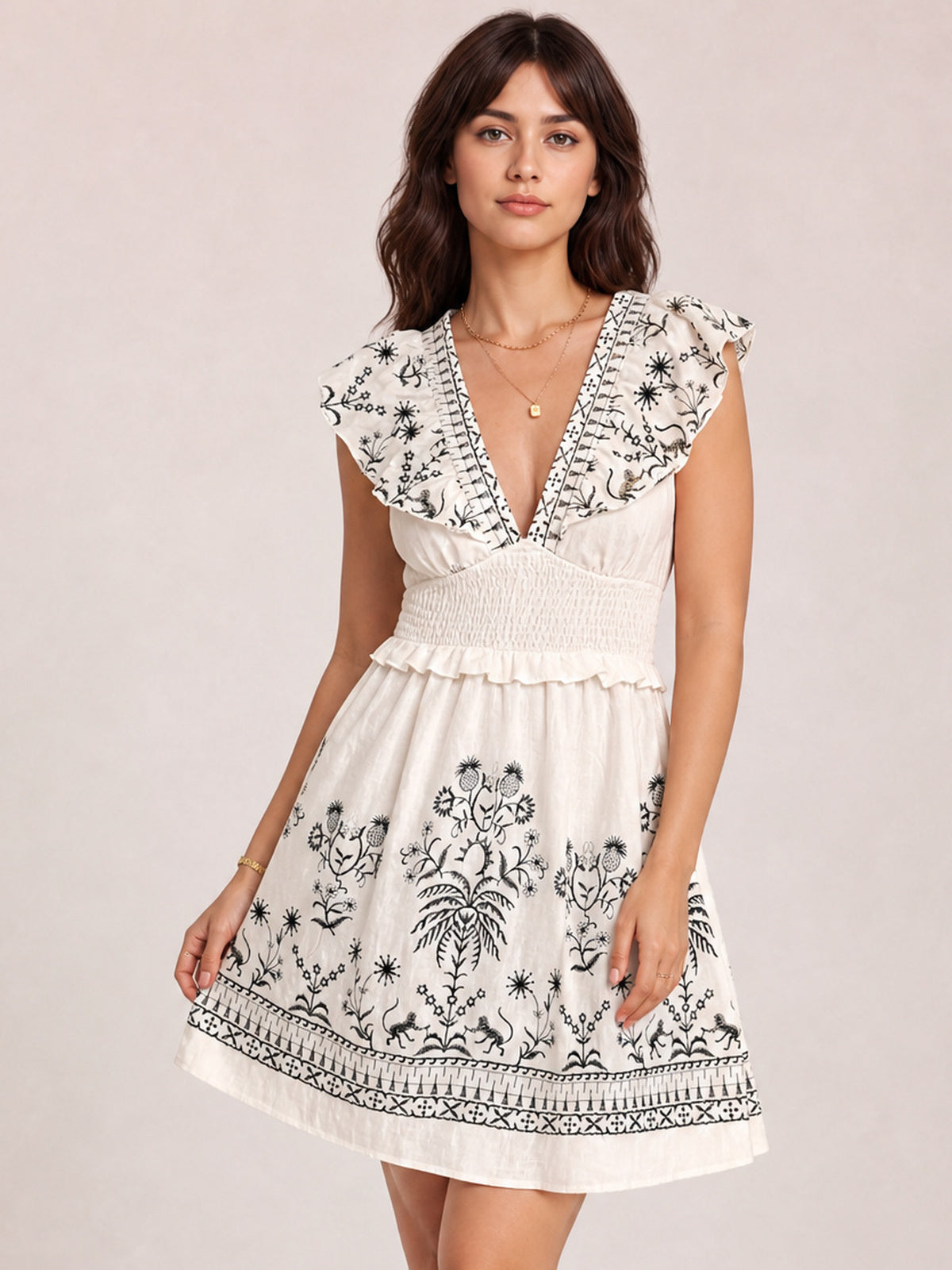 Model wears a cream floral mini dress with black botanical print, V-neckline, ruffled cap sleeves, smocked waist, flared skirt, and border hem.