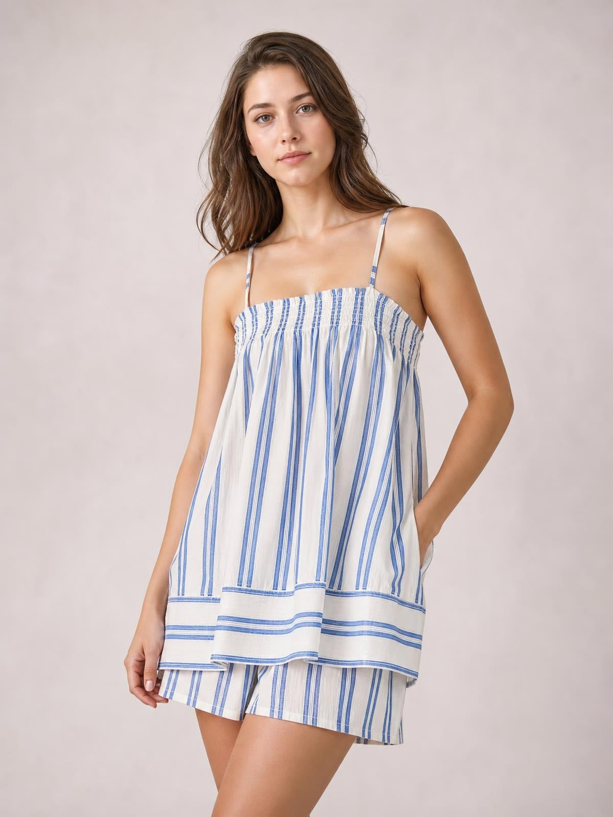 Model stands in a blue-and-white striped smocked square-neck cami and shorts set with thin straps, a relaxed silhouette, layered hem, and side pocket.