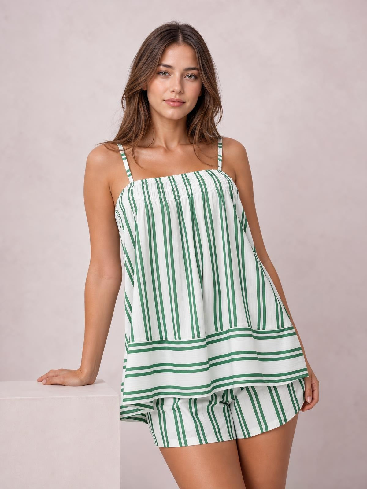 Model poses in a green and white striped smocked square neck cami and shorts set with ruched detailing, a relaxed silhouette, and pockets.