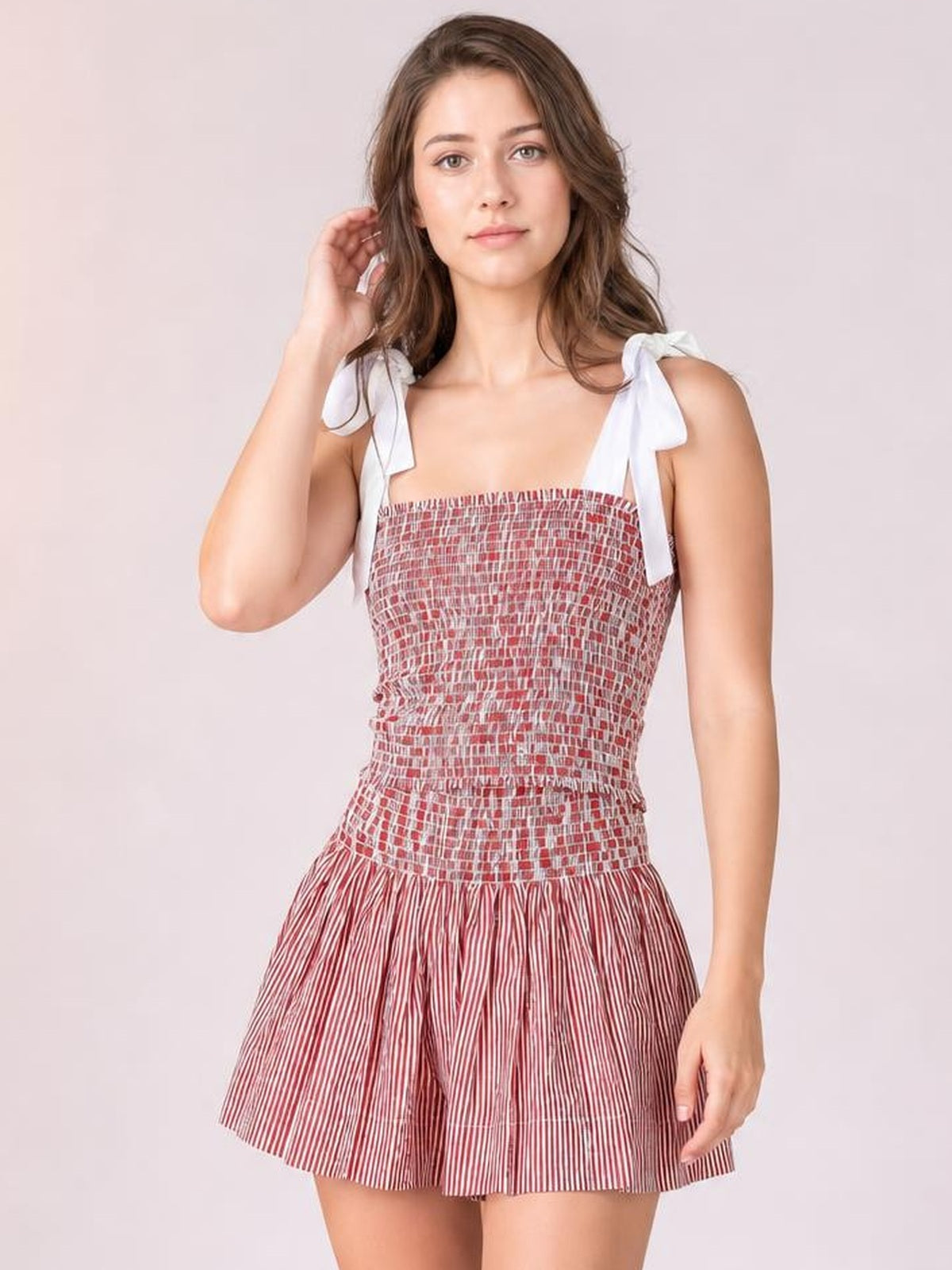 A model poses in a red-and-white smocked cami and matching flared shorts set with playful tie shoulders, a fitted bodice, and a breezy silhouette.