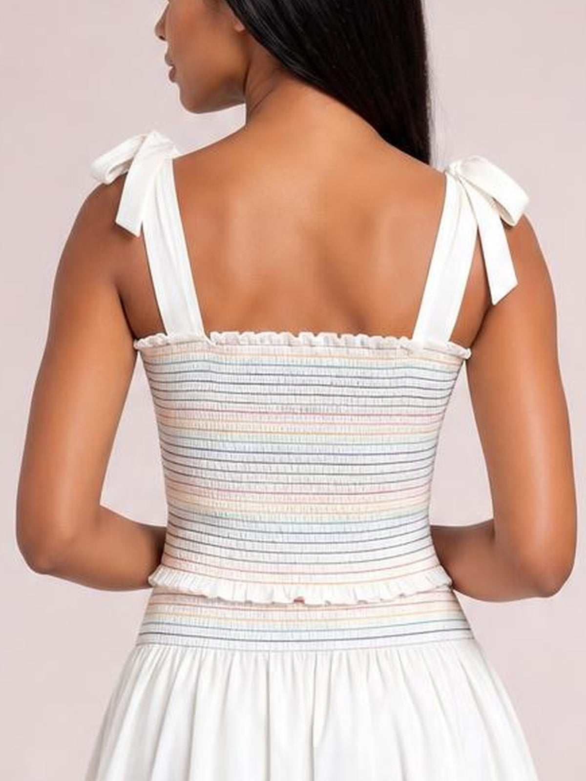 Back view of a model wearing a white smocked cami and shorts set with fine horizontal stripes, tied shoulder straps, and a relaxed silhouette.