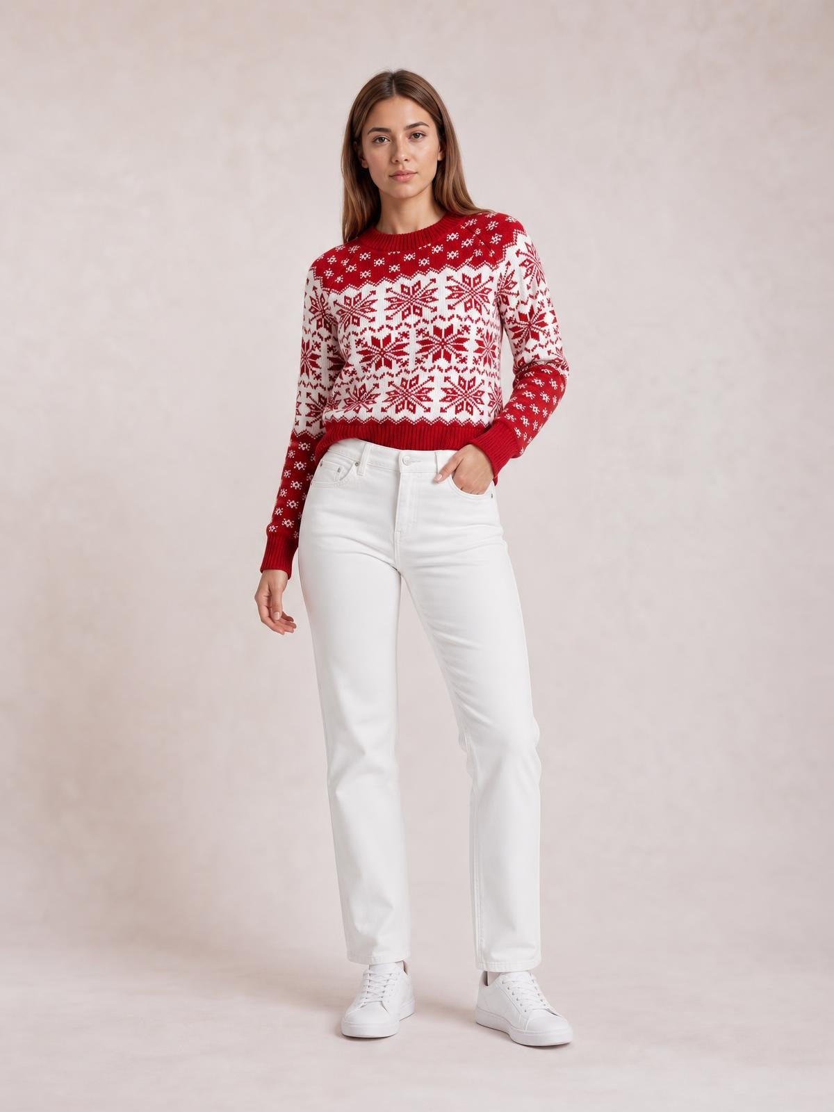 A model wears a red and white snowflake-pattern long sleeve sweater with a crew neckline, ribbed cuffs and hem, standing with one hand in her pocket.