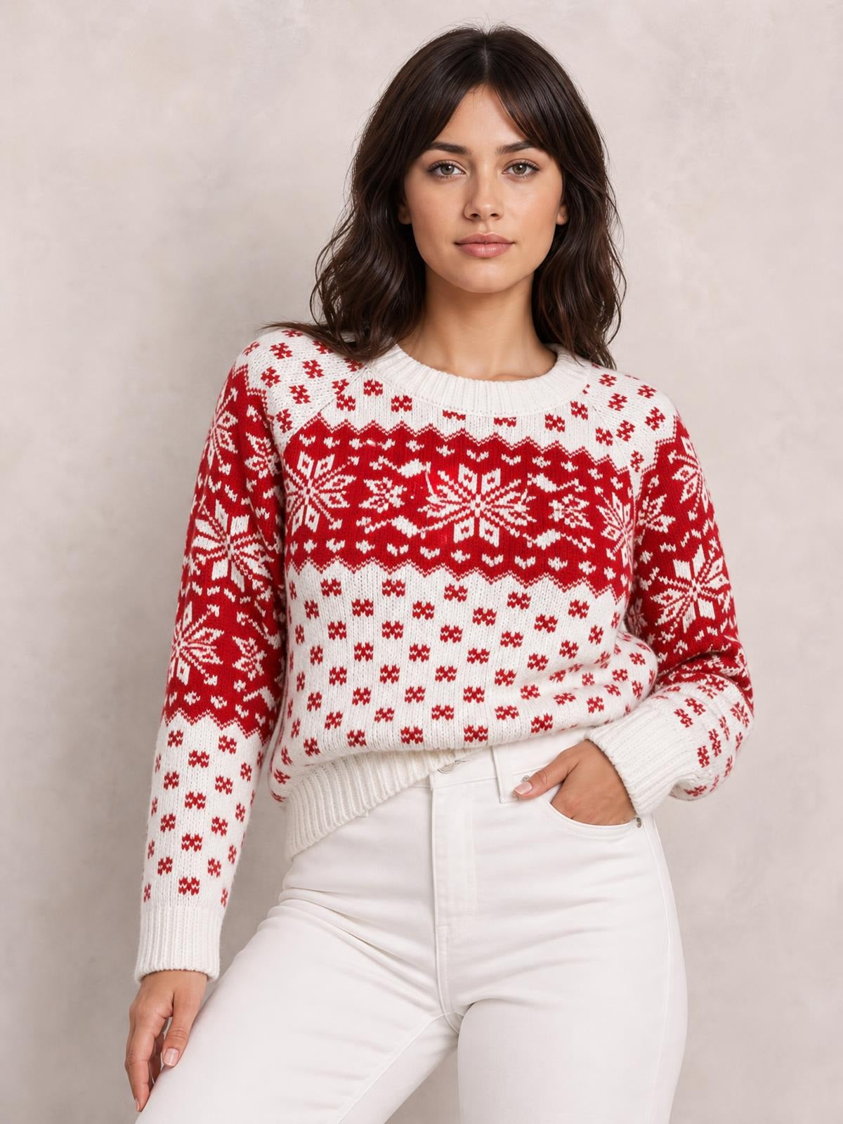 A model wears a white and red snowflake pattern long sleeve sweater with a crew neck, ribbed cuffs and hem, and relaxed silhouette, posing with one hand in her pocket.
