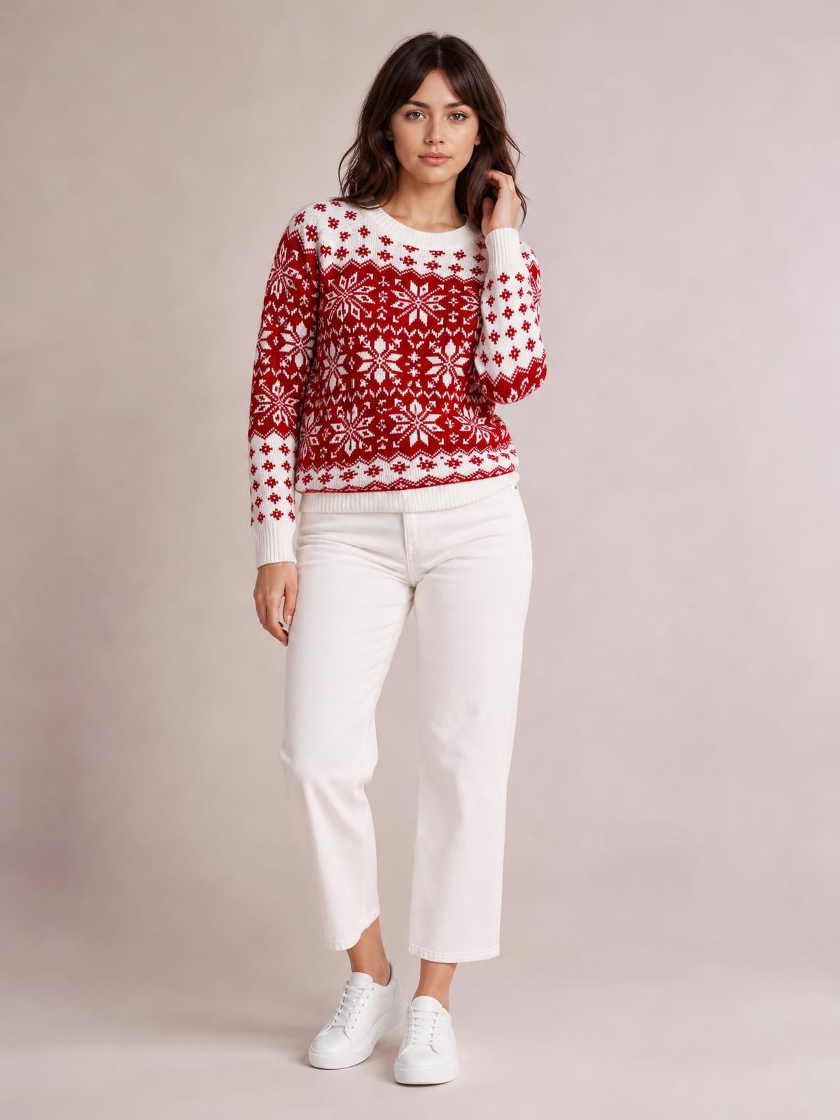 Model wearing a red and white snowflake pattern long sleeve sweater with a crew neck, ribbed cuffs and hem, standing with one hand touching her hair.