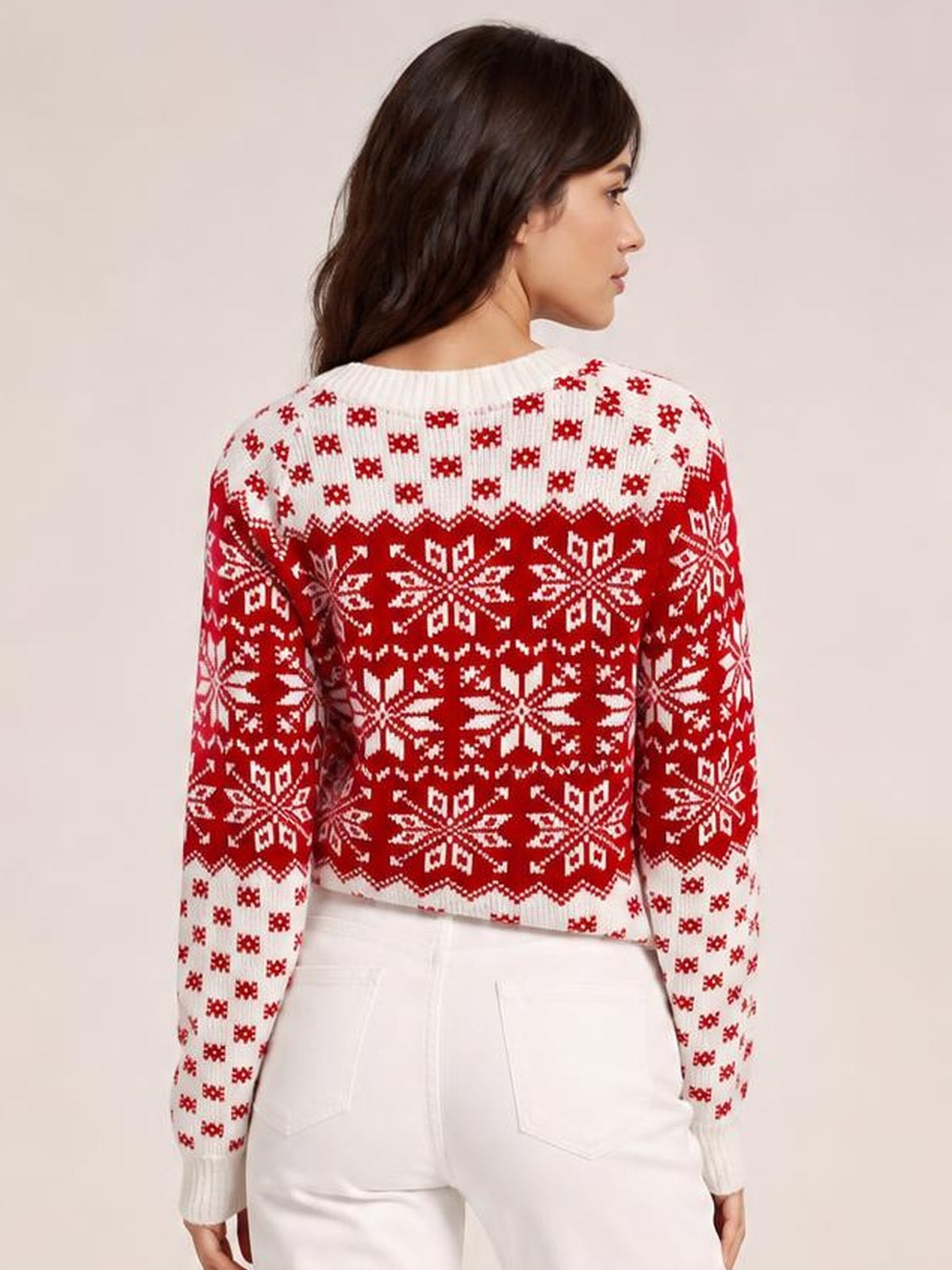 A model looks over her shoulder wearing a white long sleeve sweater with bold red snowflake patterns, ribbed neckline and cuffs, and a waist-length silhouette.