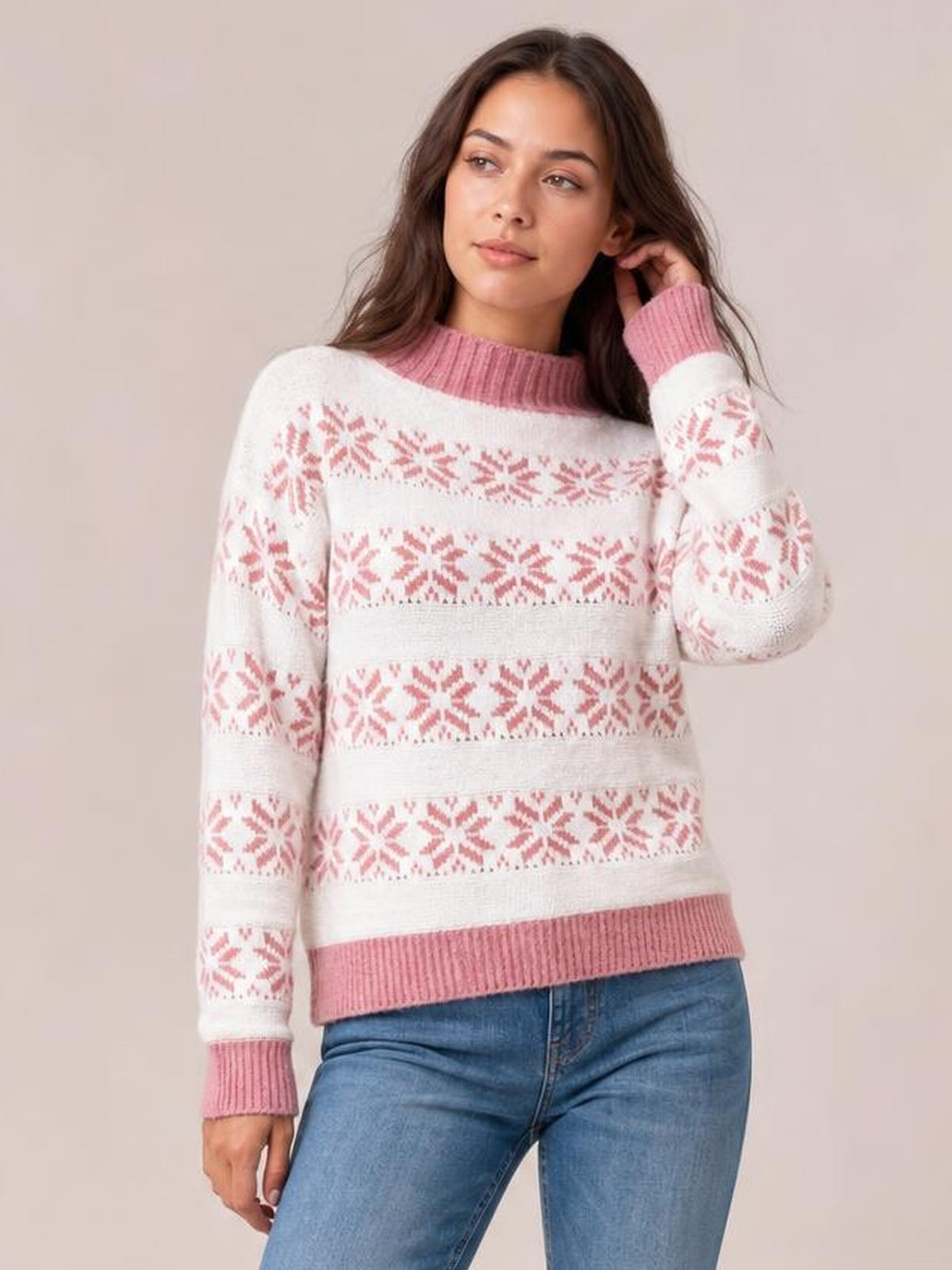 Model wearing a white snowflake pattern mock neck sweater with pink ribbed collar, cuffs, hem, and relaxed long sleeves, posing with one hand near her hair.