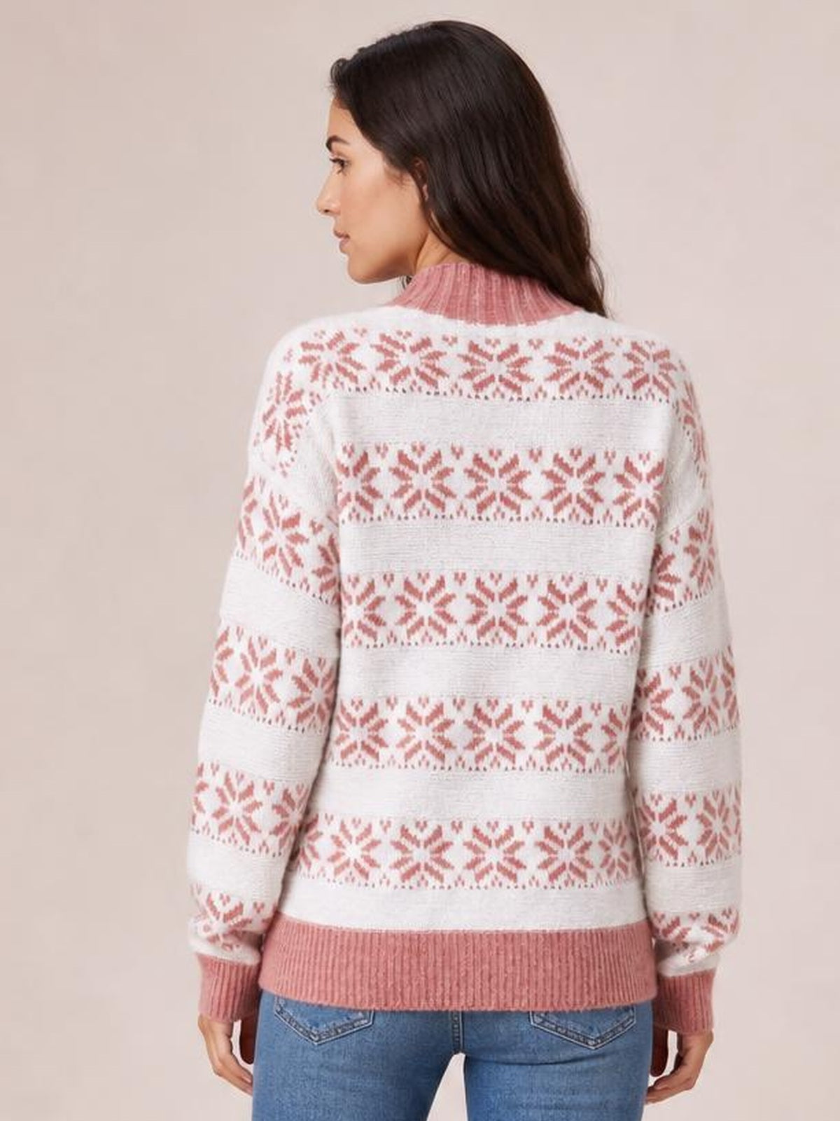 A woman viewed from behind wears a white and pink snowflake pattern mock neck sweater with long sleeves, ribbed cuffs and hem, and a relaxed silhouette.