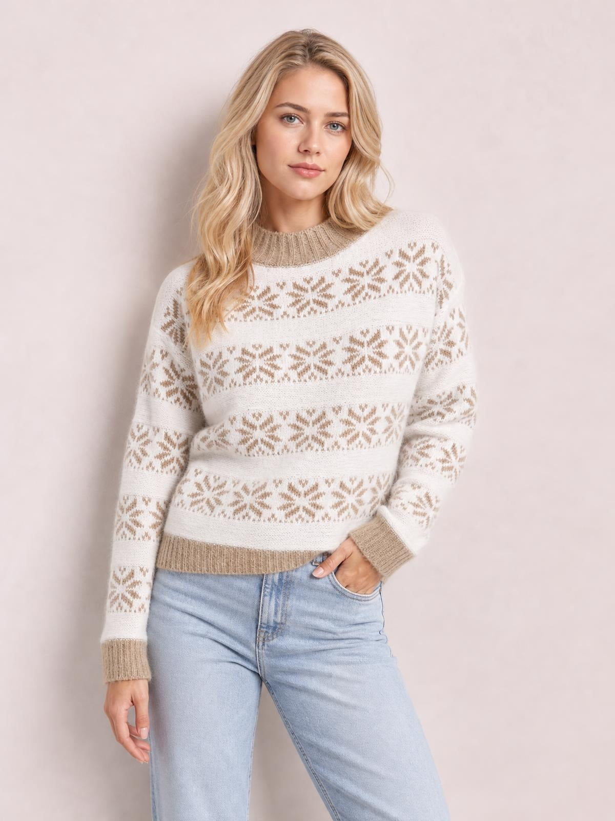 Model wears a white snowflake-pattern sweater with tan accents, long sleeves, ribbed cuffs and hem, and a relaxed silhouette while posing with one hand in her pocket.