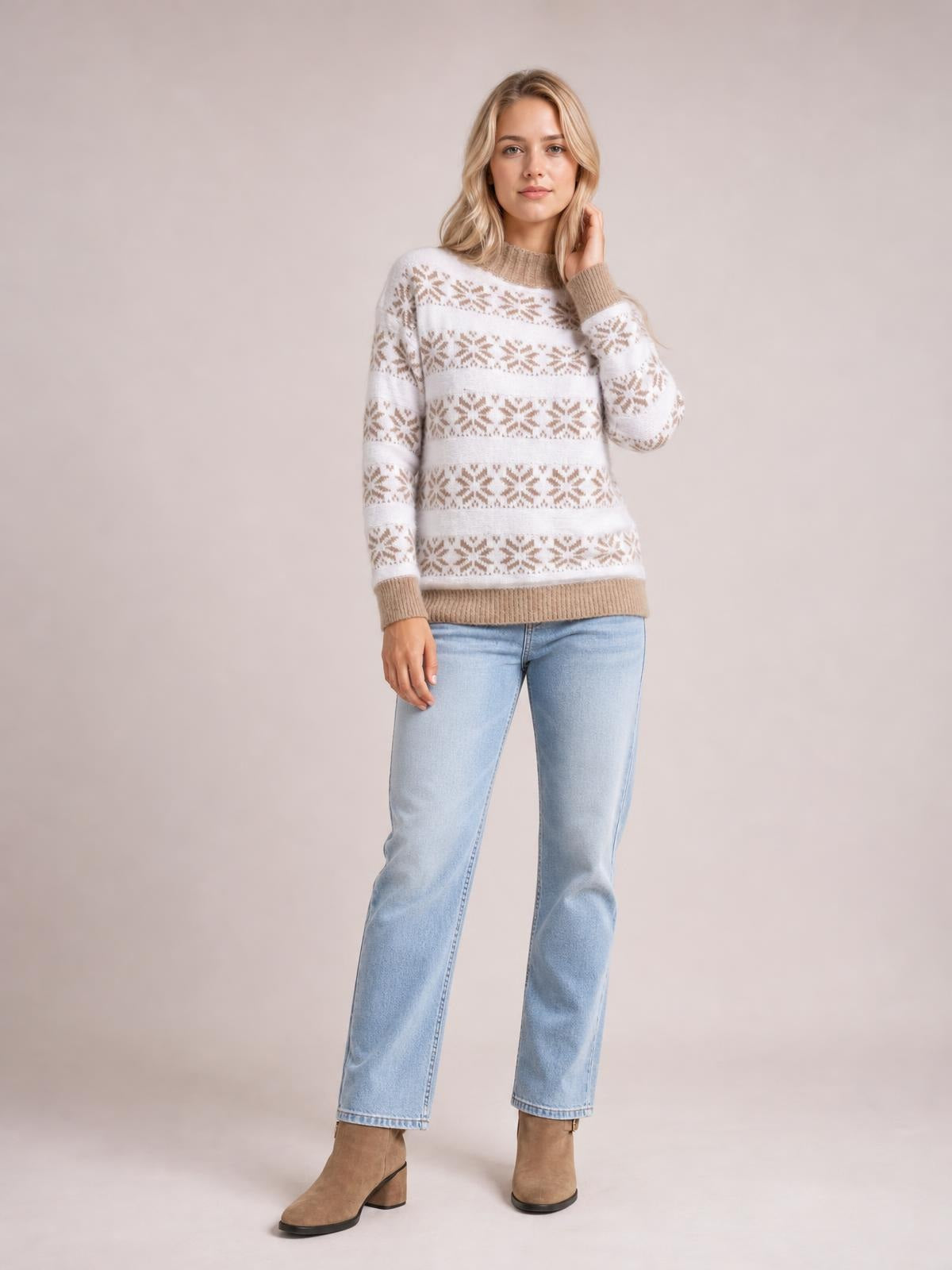 Model wearing a white snowflake pattern mock neck sweater with beige ribbed cuffs and hem, relaxed silhouette, standing with one hand touching her hair.