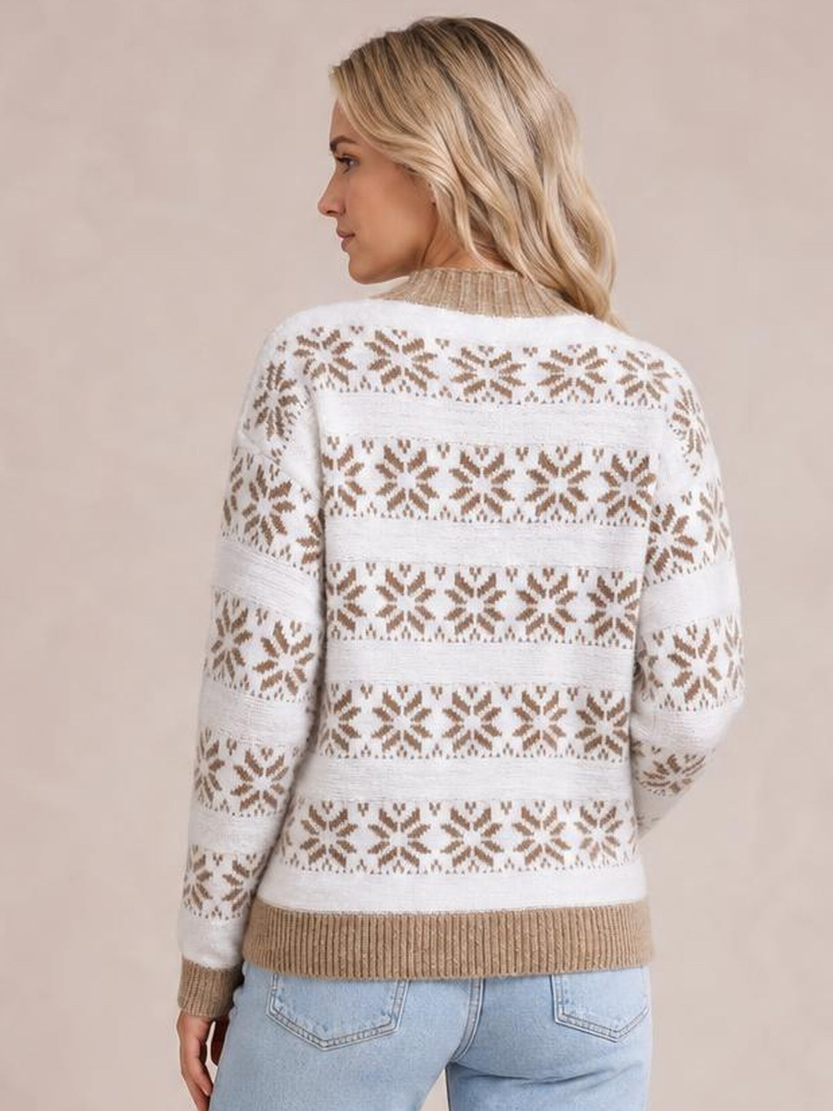 A woman looks over her shoulder wearing a white snowflake pattern mock neck sweater with brown accents, ribbed cuffs and hem, and a relaxed silhouette.