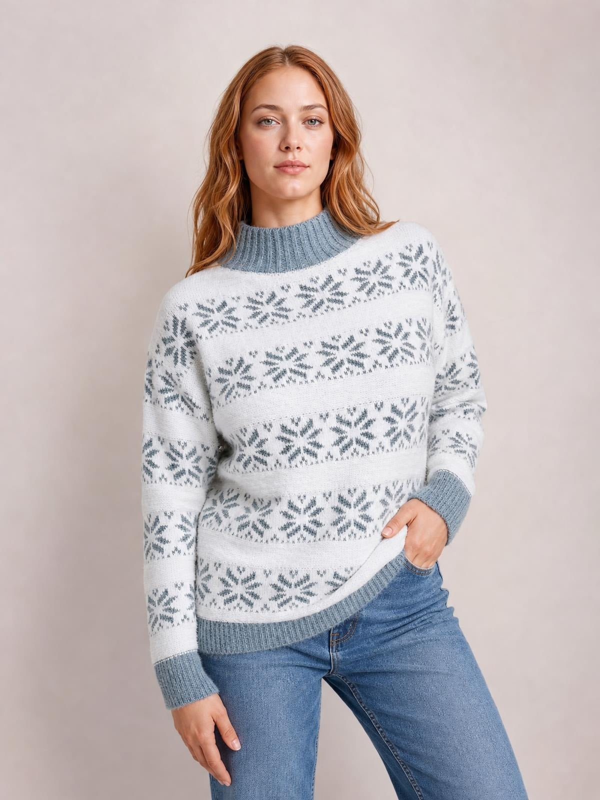 Model poses with one hand in her jeans pocket, wearing a white and gray snowflake-pattern sweater with a ribbed mock neck, cuffs, and hem.