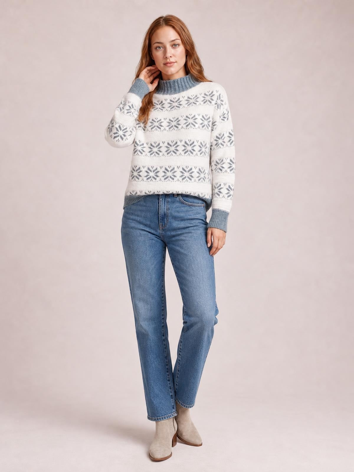 A model poses in a white snowflake pattern mock neck sweater with gray ribbed trim, long sleeves, and a relaxed straight silhouette.