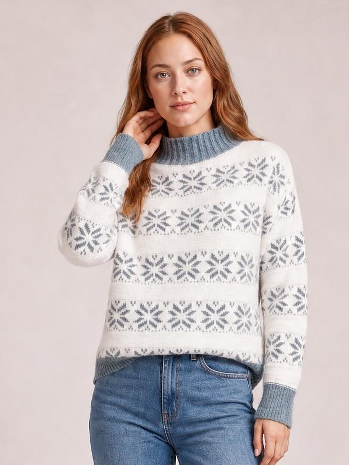Model poses in a white snowflake pattern mock neck sweater with gray ribbed collar and cuffs, long sleeves, and a relaxed silhouette.