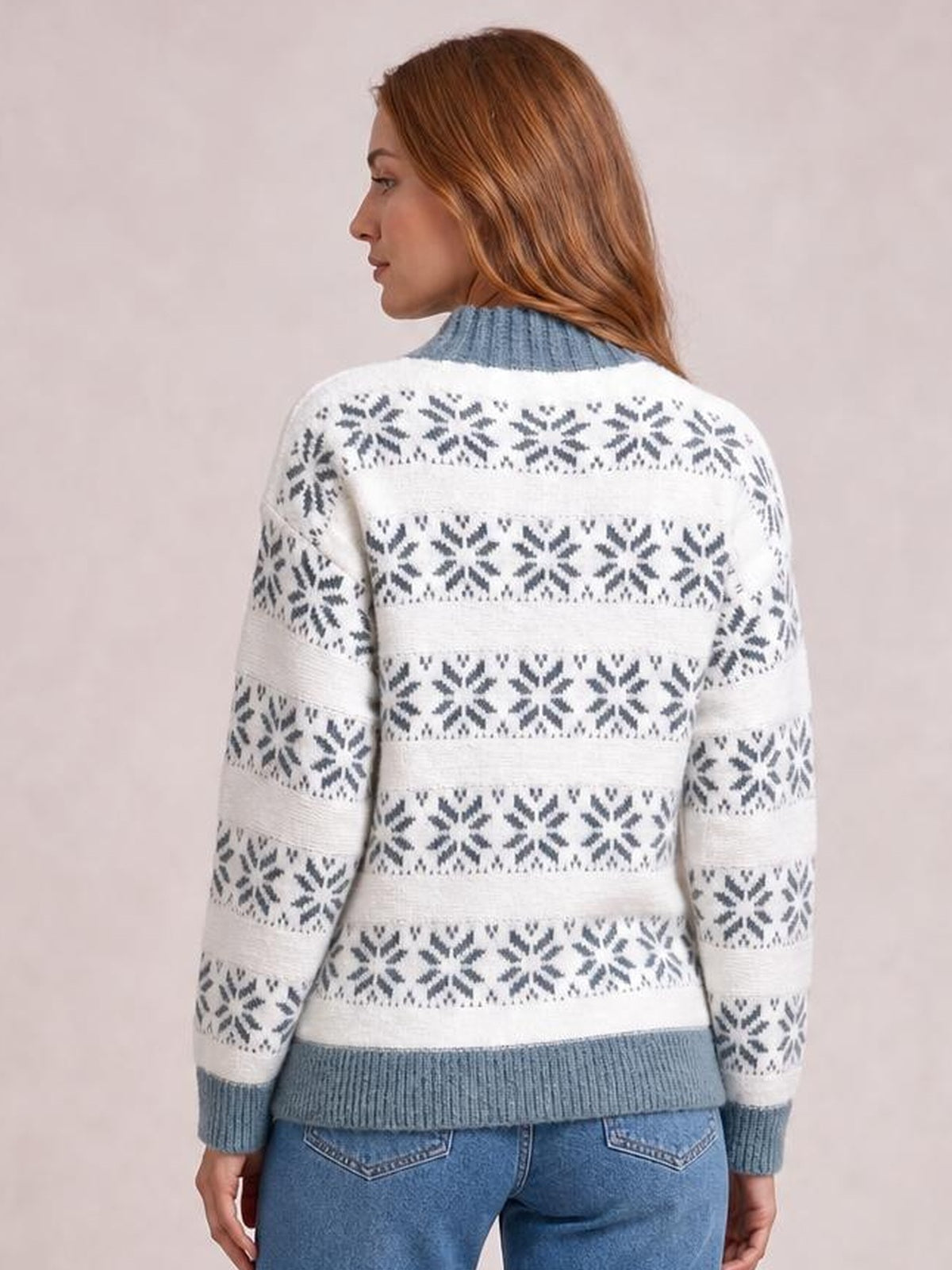 Model viewed from behind wearing a white snowflake pattern mock neck sweater with blue ribbed collar, cuffs, hem, and a relaxed long-sleeve silhouette.