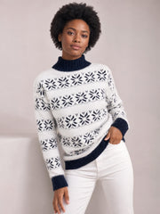 Model poses in a white snowflake pattern mock neck sweater with navy ribbed trim, long sleeves, and a relaxed silhouette.