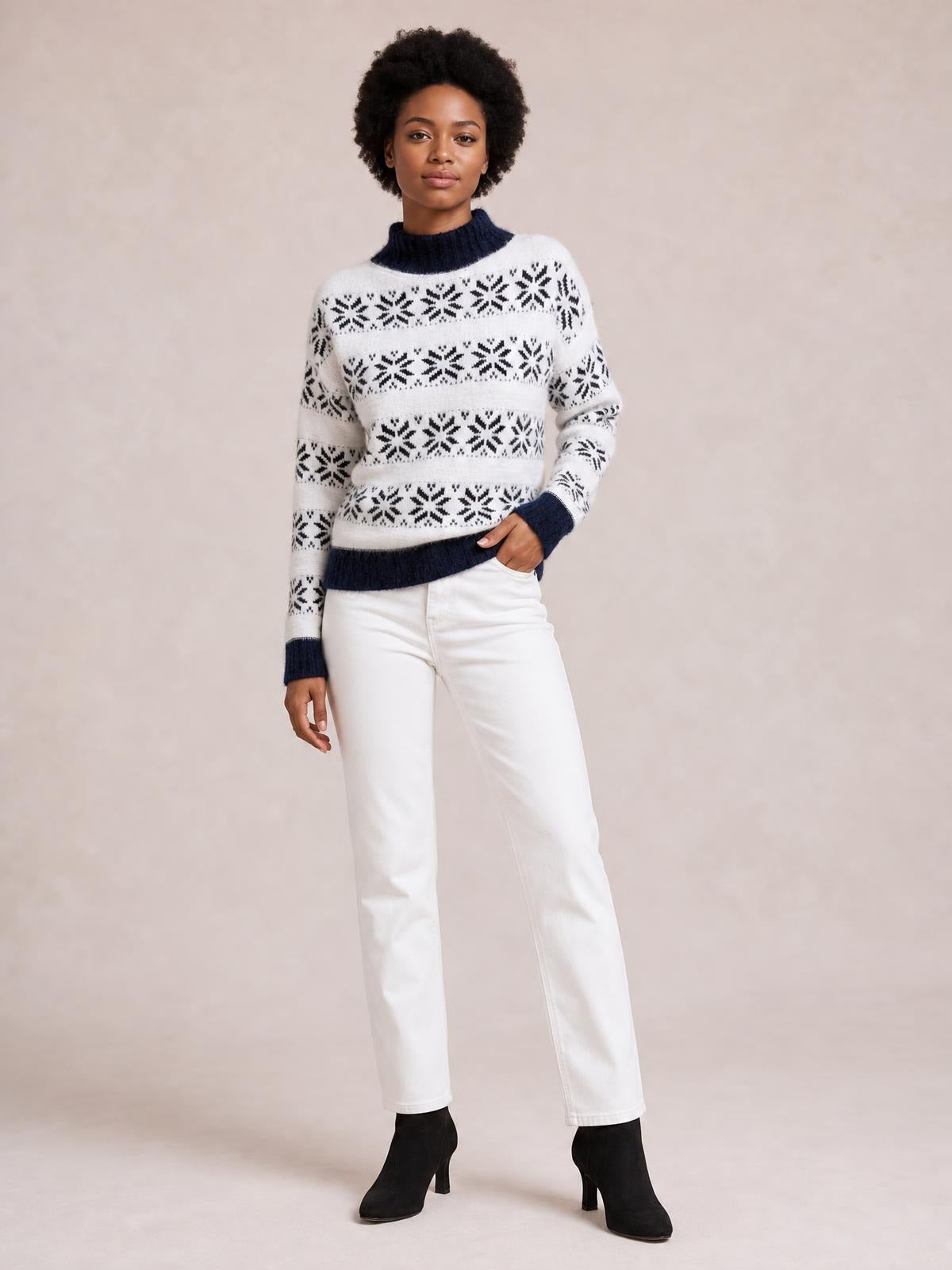 Model poses in a white snowflake-pattern sweater with a navy mock neck, ribbed cuffs and hem, long sleeves, and a relaxed silhouette.