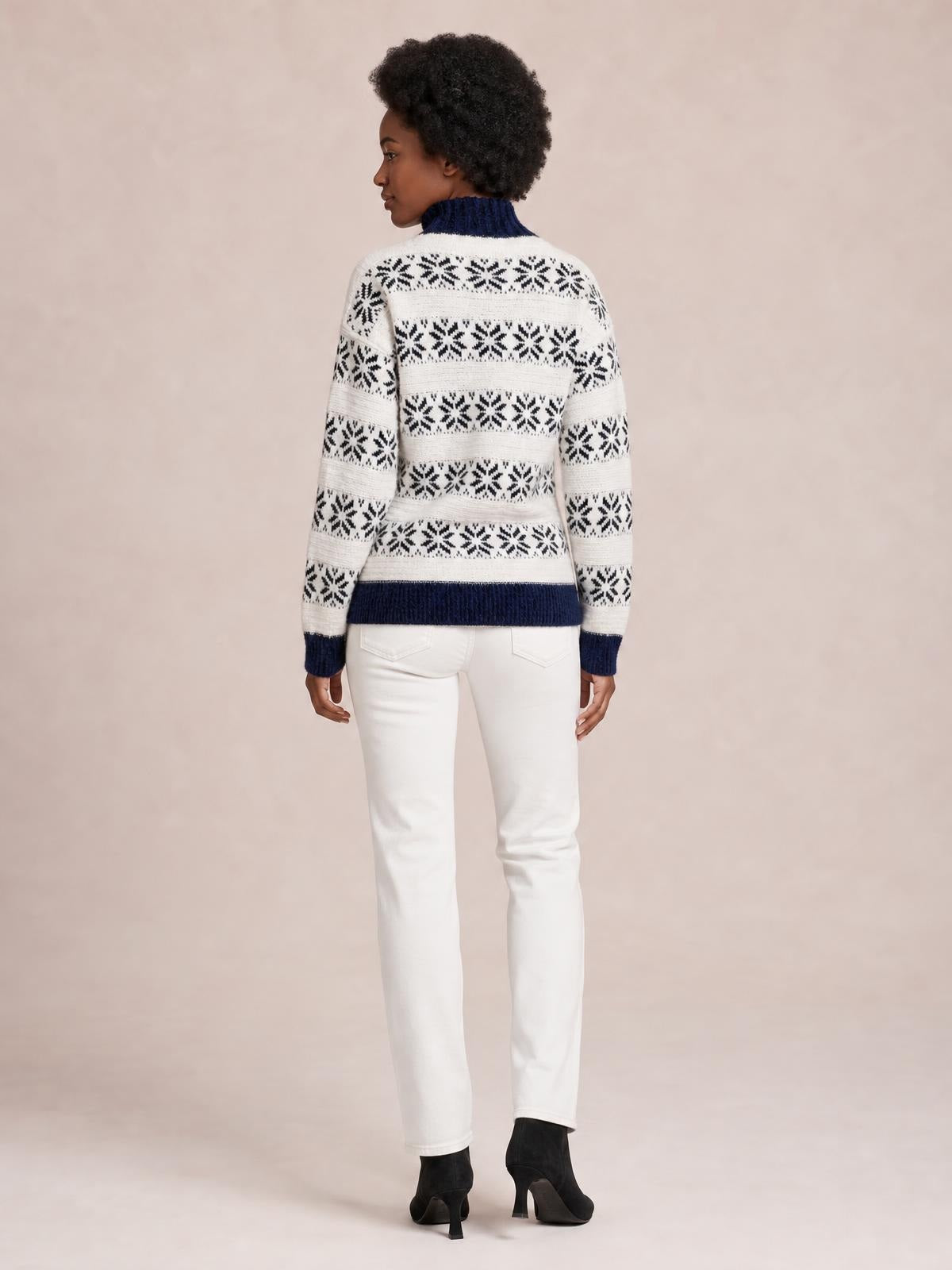 Model shown from the back in a white snowflake pattern mock neck sweater with navy ribbed collar, cuffs, hem, and a straight silhouette.