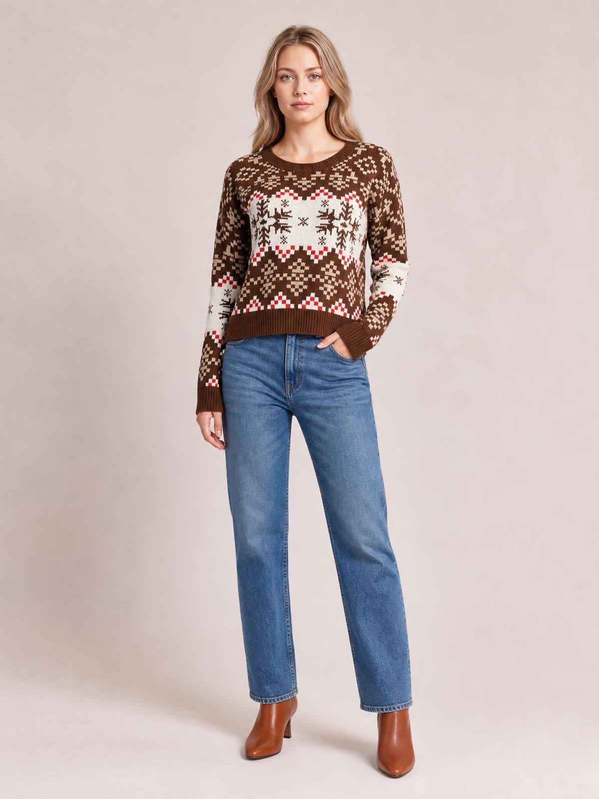 A model wears a brown snowflake-patterned round-neck sweater with long sleeves, ribbed cuffs and hem, and a relaxed silhouette, posing with one hand in her jeans pocket.