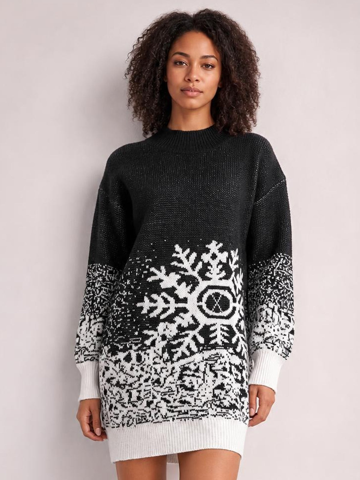 Model wears a black ribbed snowflake pattern sweater dress with an oversized silhouette, long sleeves, white contrast cuffs, hem, and winter motif.