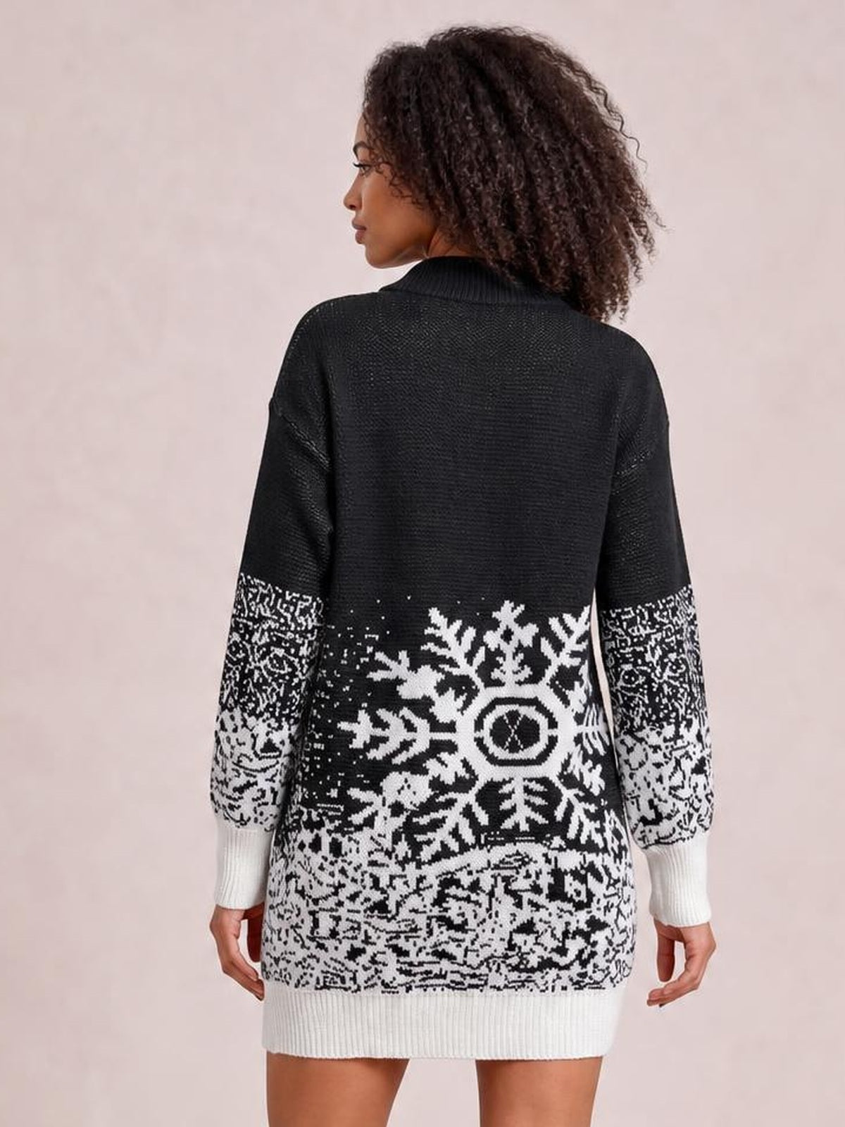 A model turned away wears a black-and-white snowflake pattern sweater dress with a relaxed silhouette, ribbed high collar, cuffs, and hem.