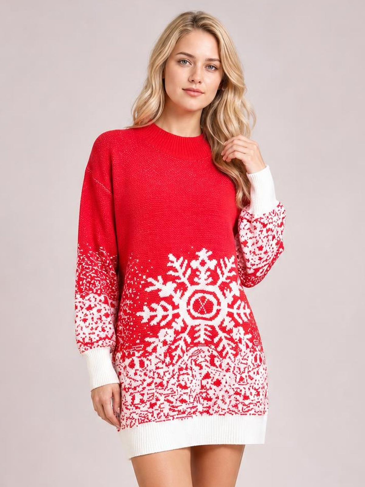 Model in a relaxed pose wears a red ribbed sweater dress with white snowflake and winter-pattern detailing, long sleeves, crew neckline, and a straight silhouette.