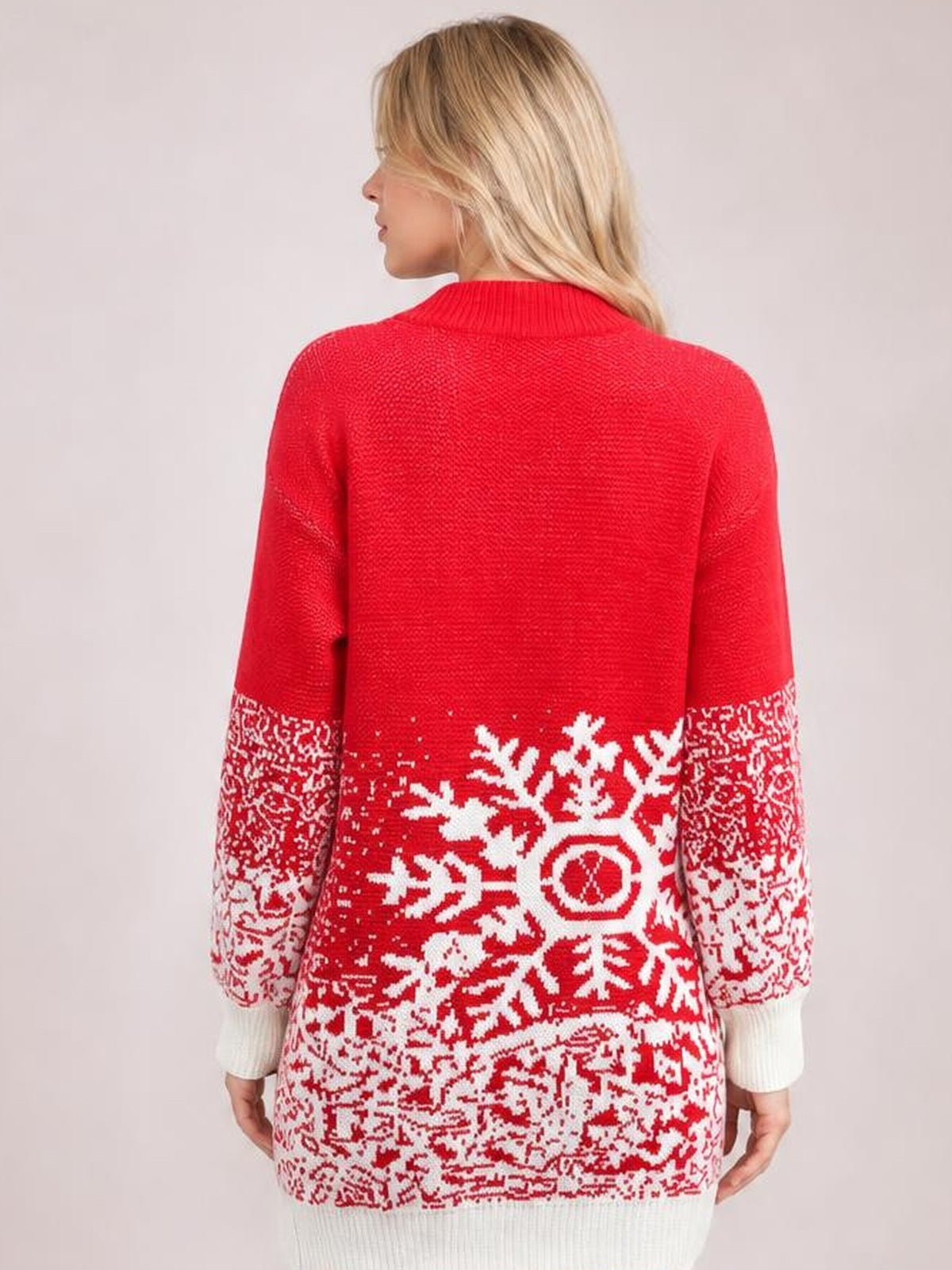 Model shown from the back wears a red snowflake-pattern sweater dress with a relaxed silhouette, ribbed high neckline, long sleeves, and white cuffs.