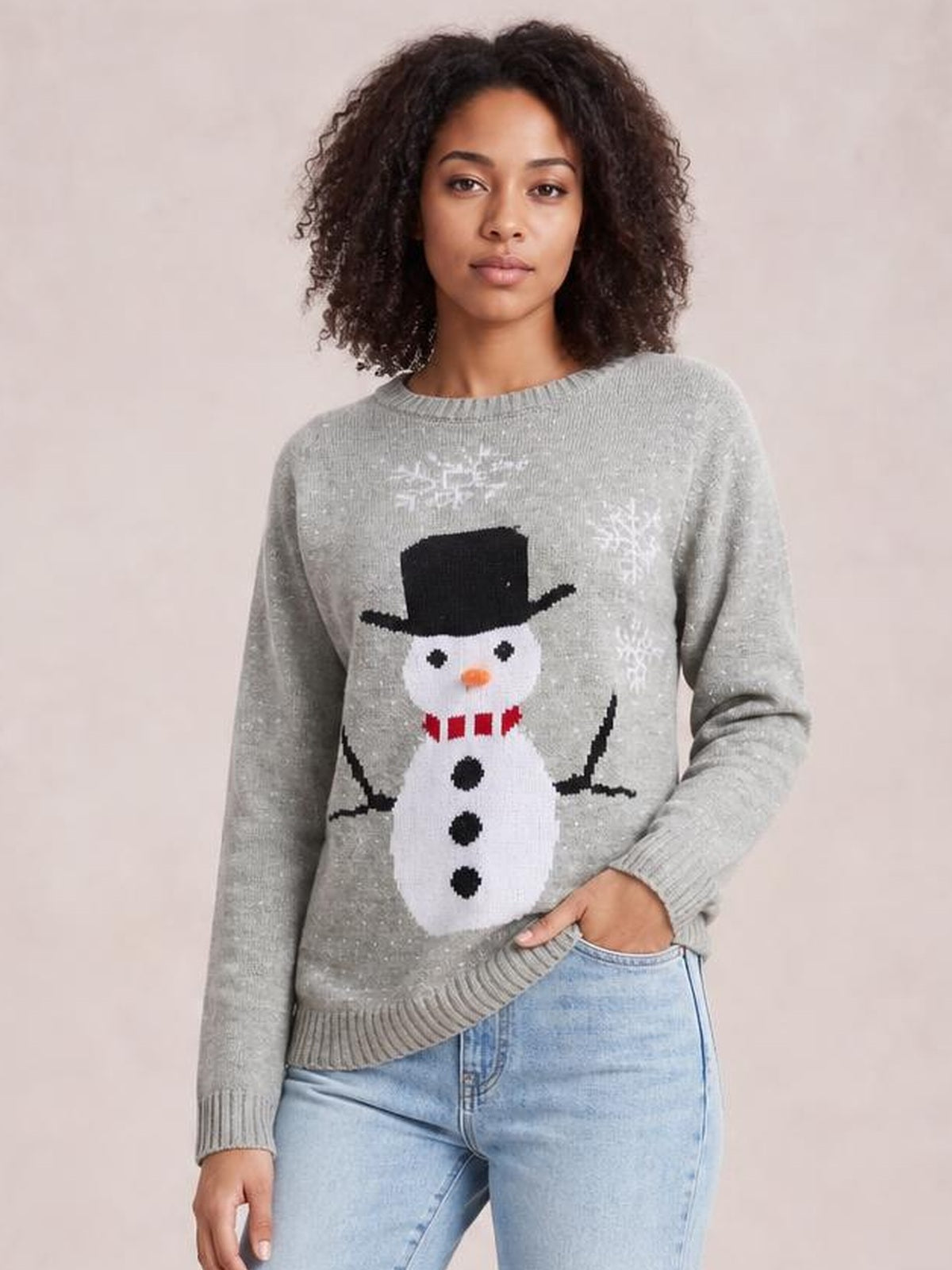 Model wearing a relaxed gray raglan sleeve sweater with ribbed trim and a festive snowman graphic, standing with one hand in her jeans pocket.