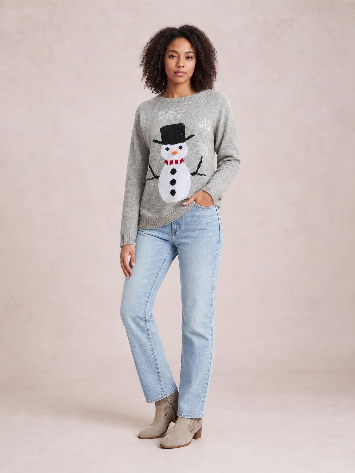 Model wearing a gray snowman graphic raglan sleeve sweater with a relaxed silhouette, ribbed crew neckline, cuffs and hem, posing with one hand in her jeans pocket.