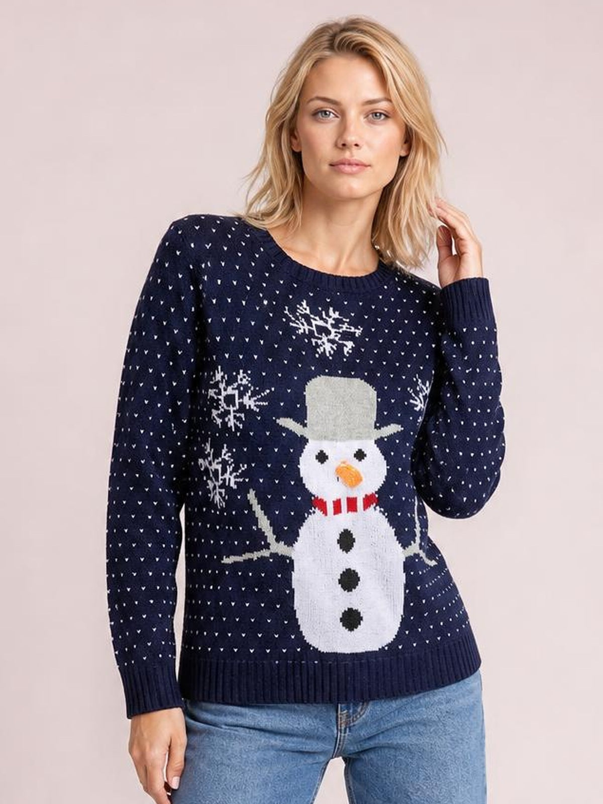 A model stands in a navy snowman graphic raglan sleeve sweater with a relaxed silhouette, ribbed crew neckline and cuffs, touching her hair with one hand.