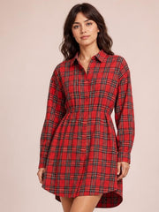 Model poses in a red checker plaid shirt dress with long sleeves, button-up front, chest pocket, fitted waist, and curved shirttail hem.