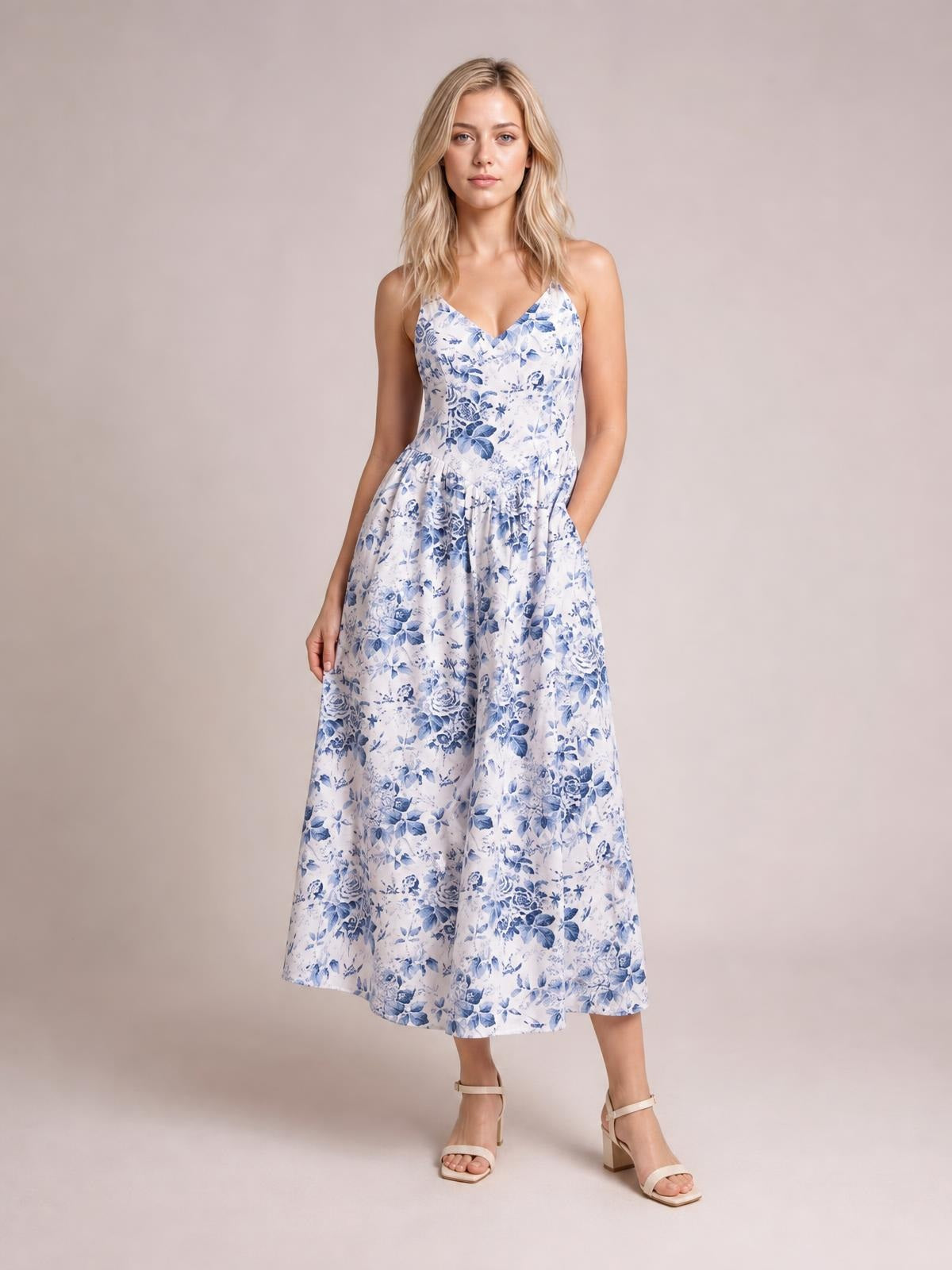 Model wears a blue and white floral woven dress with a V-neck, fitted bodice, gathered waist, and flowing midi-length A-line skirt.
