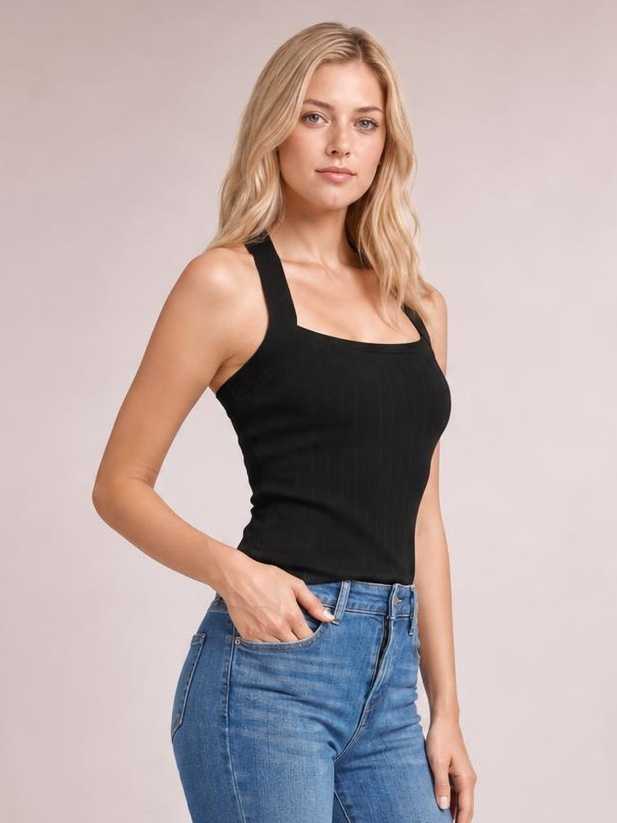 Model poses with one hand in her jeans pocket wearing a solid black knit cami with wide shoulder straps, a straight neckline, and fitted silhouette.