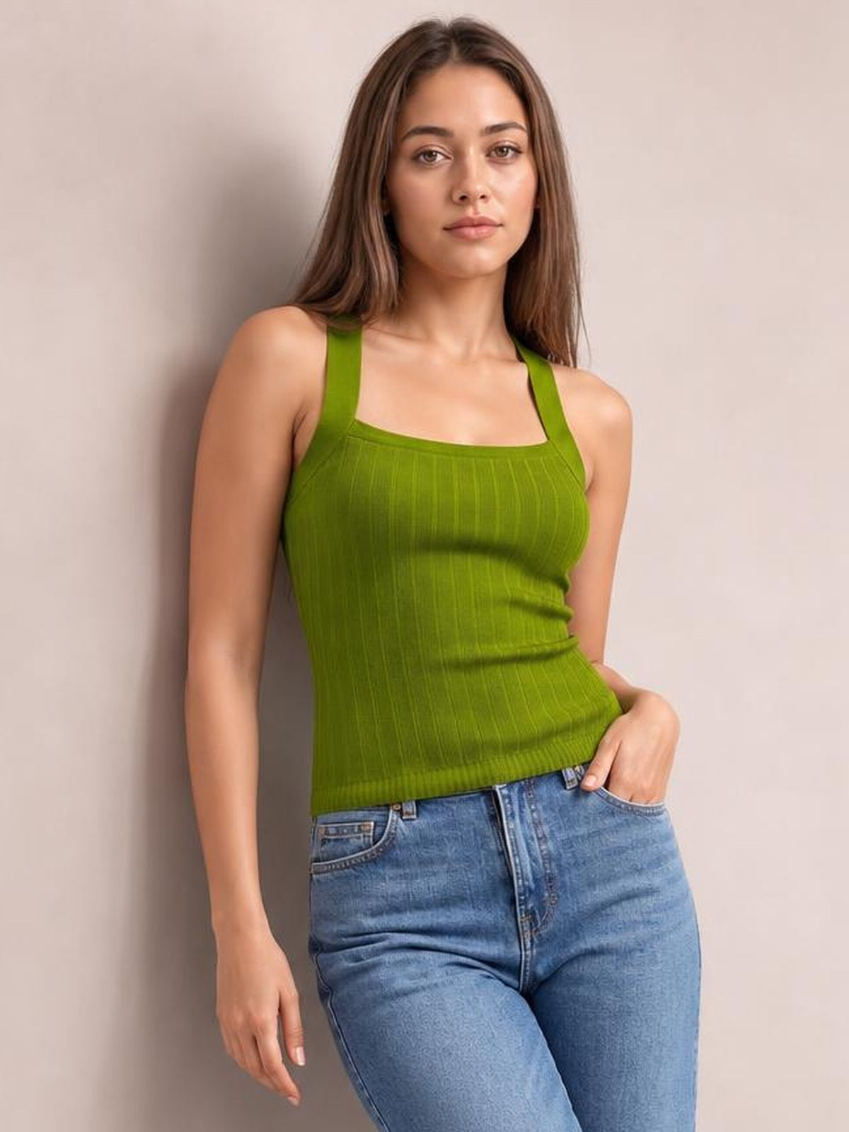 Model wearing a solid olive-green knit cami with wide straps, a square neckline, ribbed construction, and a fitted silhouette, posing with one hand in her jeans pocket.