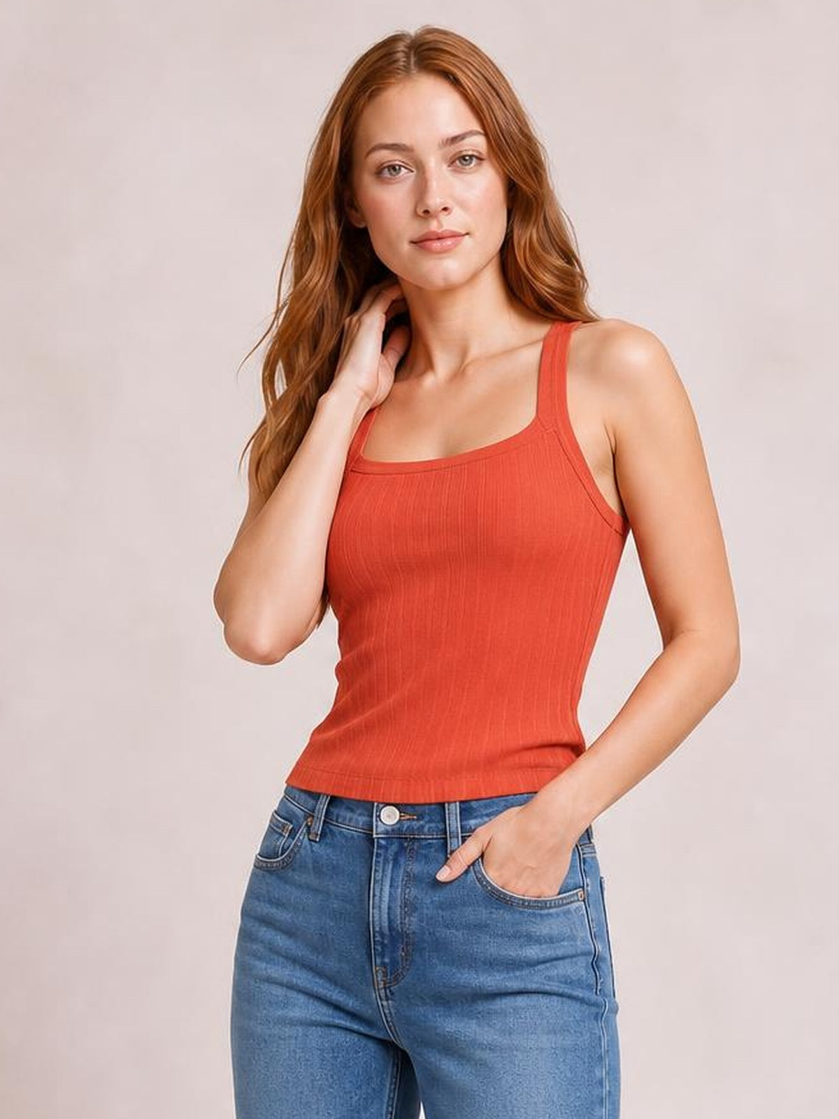 Woman poses in a solid coral-red knit cami with wide shoulder straps, a square neckline, subtle ribbed texture, and a fitted sleeveless silhouette.