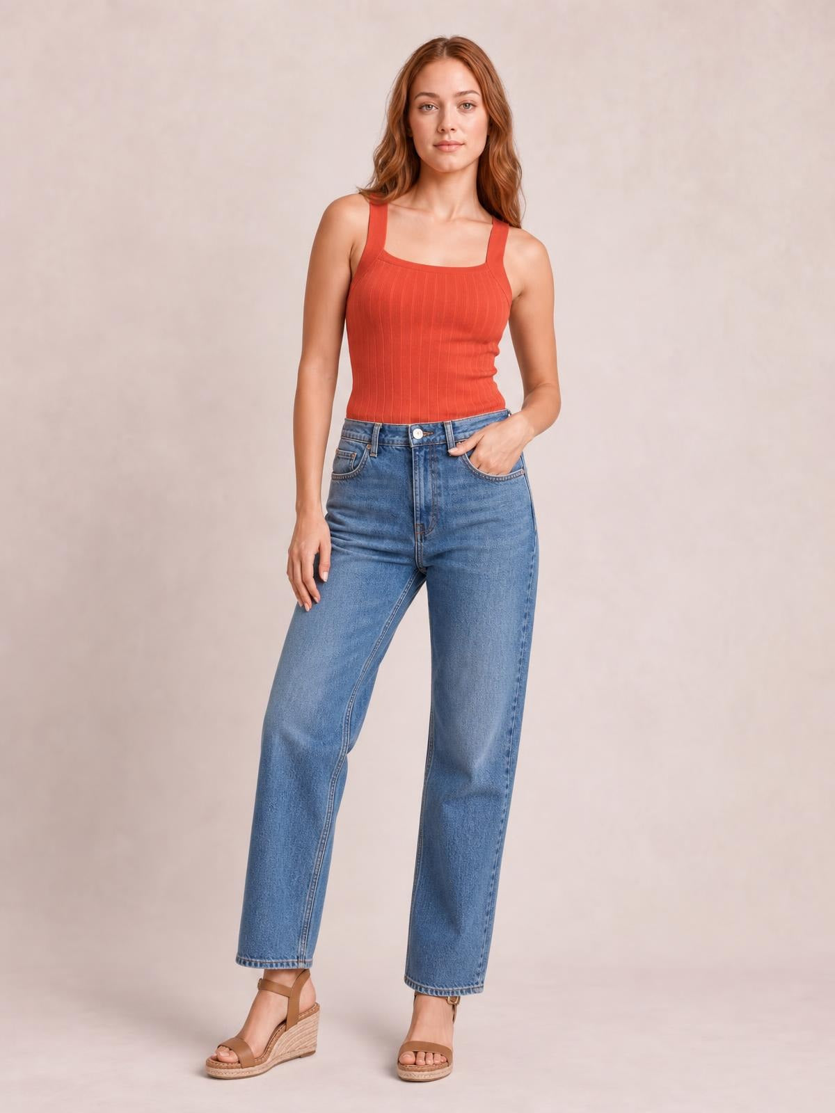 A model poses in a solid coral knit cami with a square neckline, wide straps, vertical ribbed texture, and a fitted silhouette.