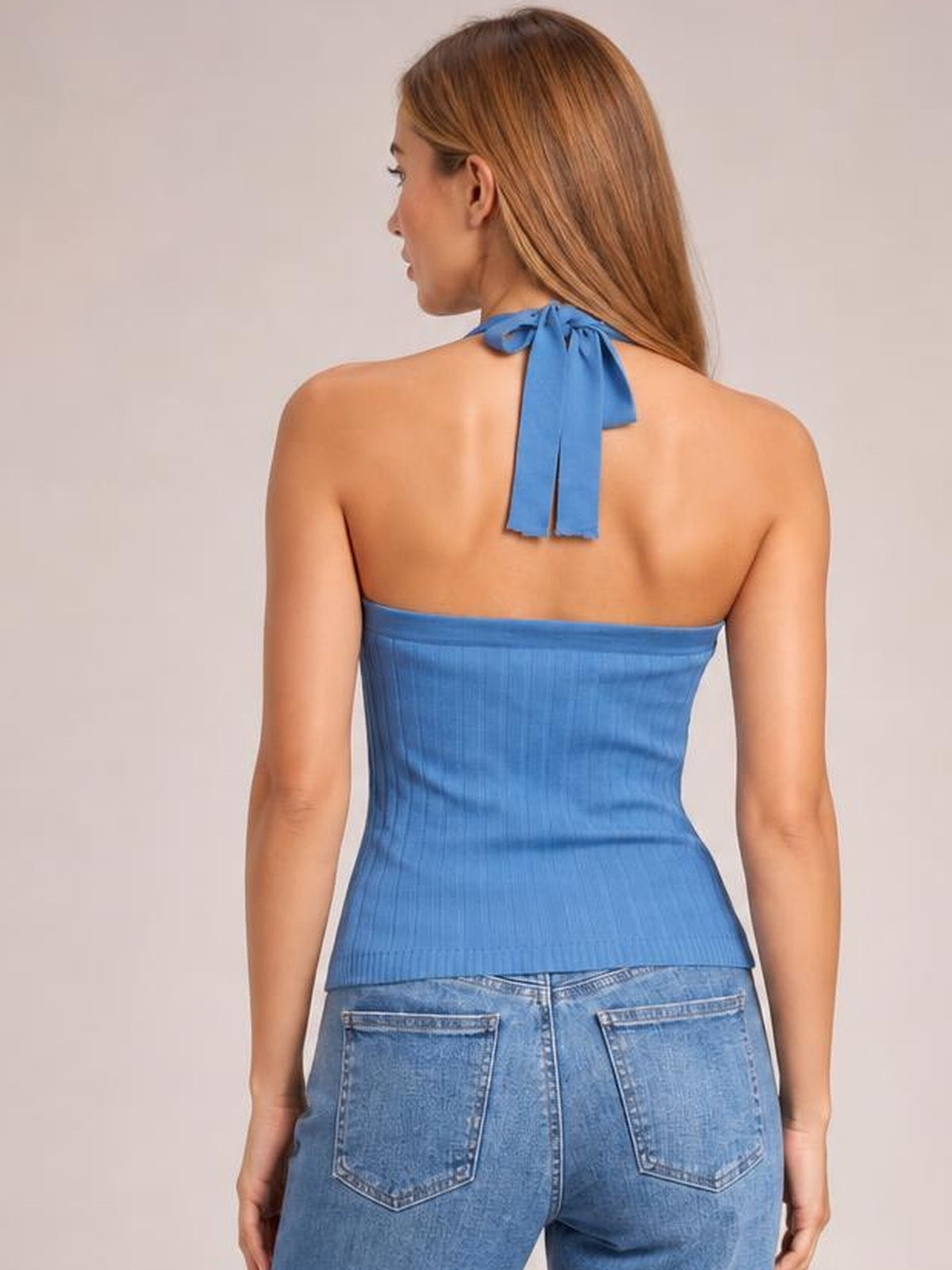 Model shown from behind wearing a solid blue halter neck knit cami with a tied neck, ribbed texture, fitted waist, and straight hem.
