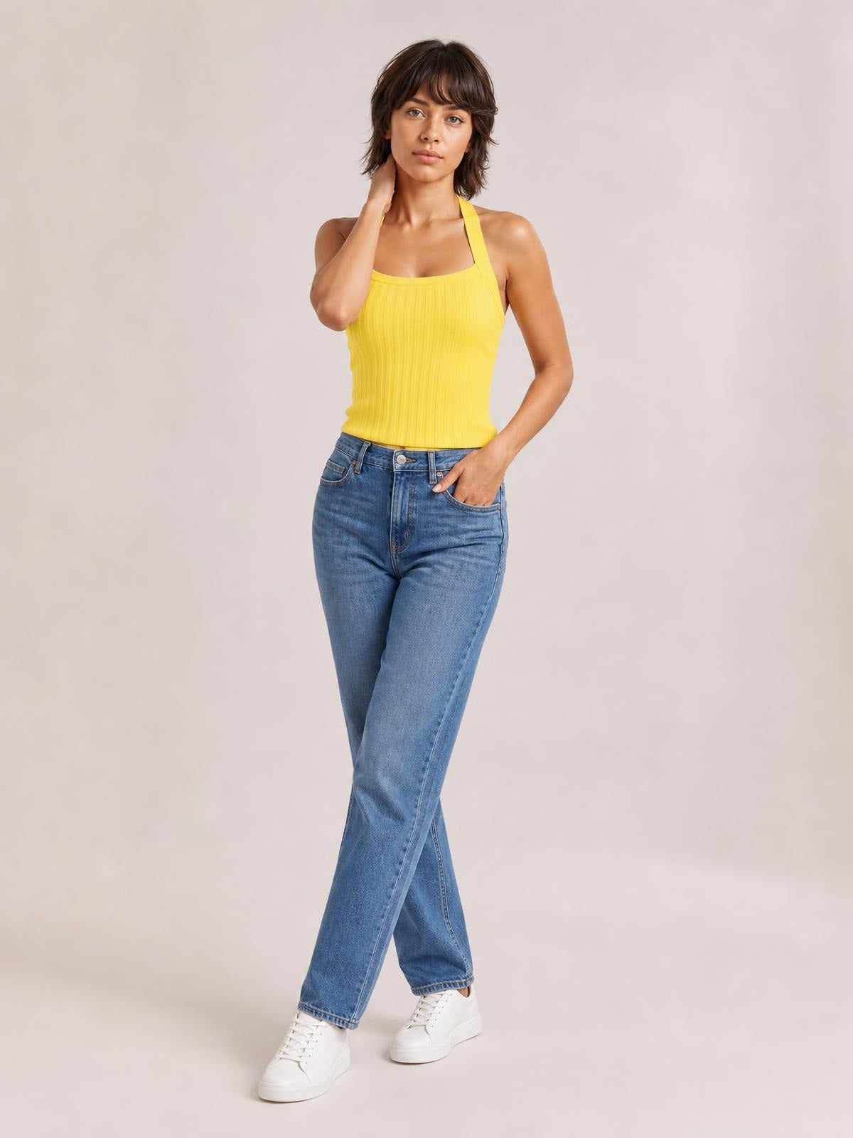 Model wears a bright yellow solid-color halter neck knit cami with a fitted silhouette and vertical ribbed texture, posing with one hand at her neck.