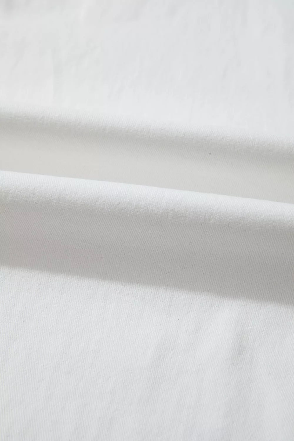 Close-up of solid-color white casual jeans fabric showing a fine diagonal twill weave and softly folded cotton-blend construction.