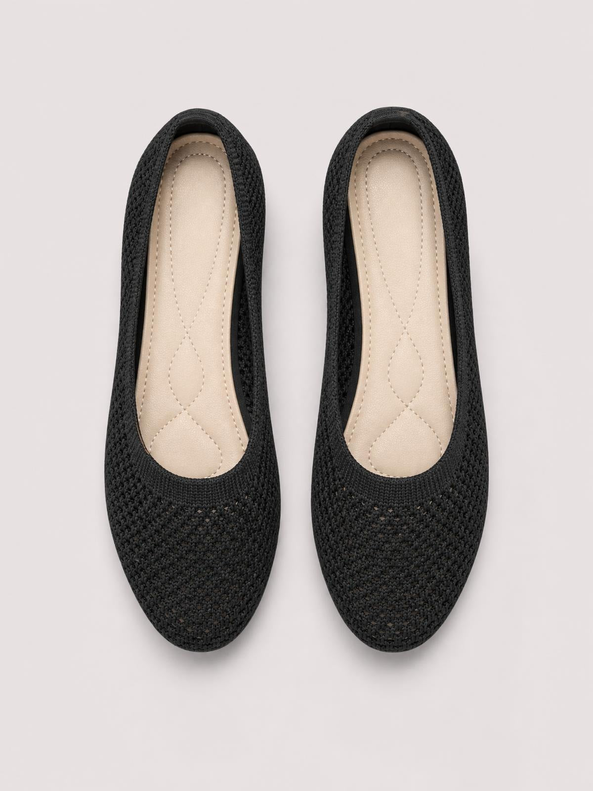 Pair of solid black mesh flat slip-ons with rounded toes, low heels, textured uppers, and beige stitched insoles.
