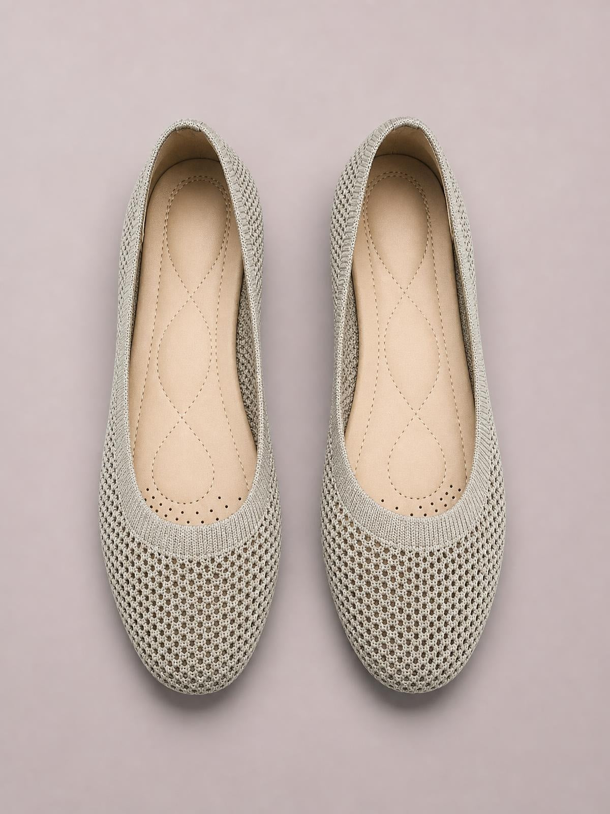 Pair of solid-color beige mesh flat slip-ons with rounded toes, low heels, knitted uppers, and cushioned stitched insoles.
