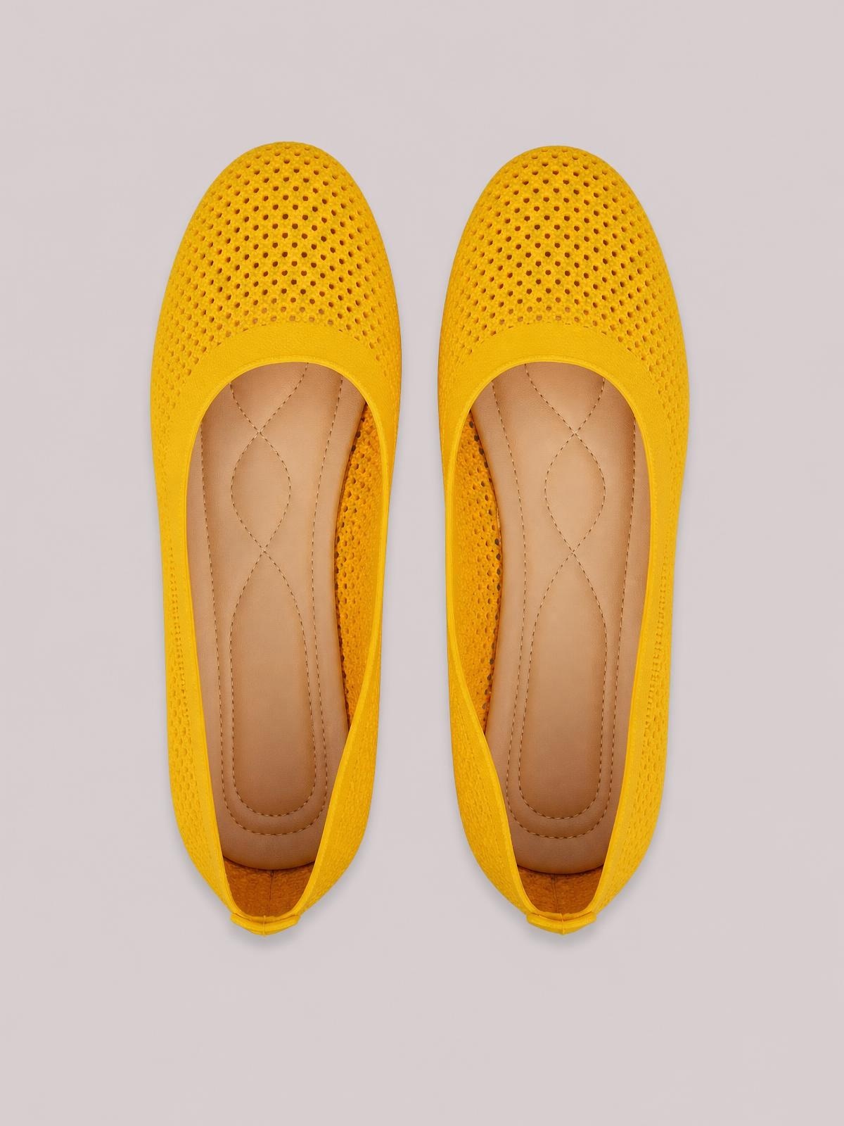 Bright yellow mesh flat slip-on shoes with perforated uppers, rounded toes, low heels, tan cushioned insoles, and rubber soles.