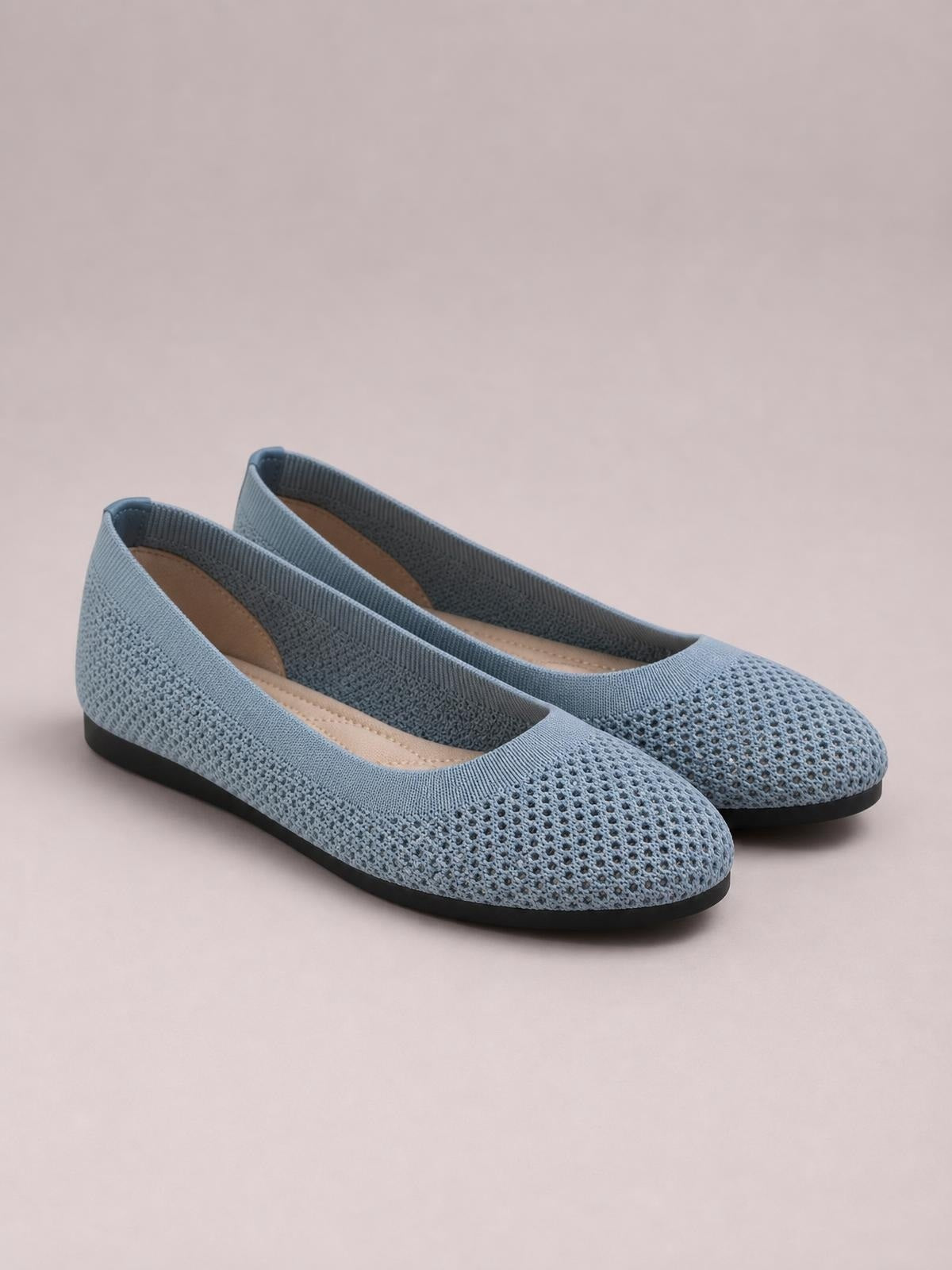 Blue-gray solid color mesh flat slip-ons feature rounded toes, elasticized openings, cushioned insoles, and low black rubber soles.