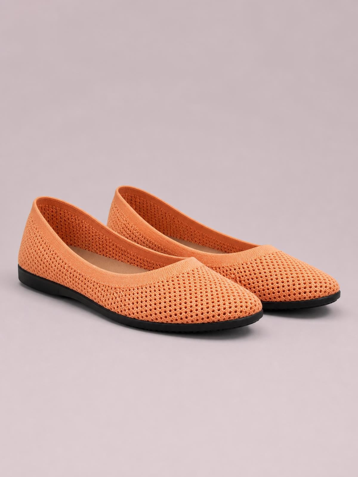 Solid orange mesh flat slip-ons feature rounded toes, low-profile black rubber soles, and a breathable open-knit construction.