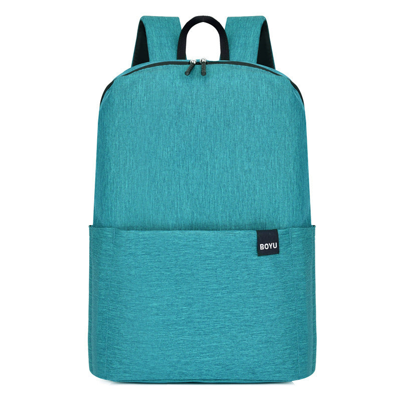Solid teal nylon backpack with a streamlined medium silhouette, rounded corners, gently curved base, top zip closure, exterior slip pocket, grab handle, and shoulder straps.