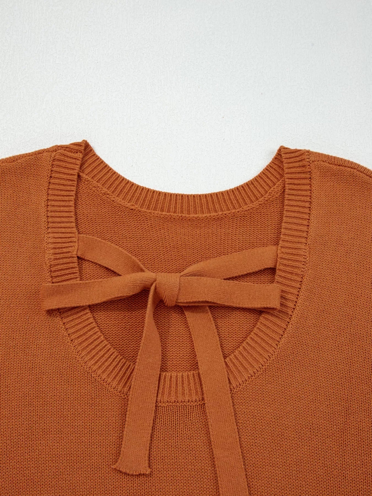 Rust-colored sweater featuring a ribbed crew neckline, drop-shoulder construction, and a front tie bow with long knit straps.