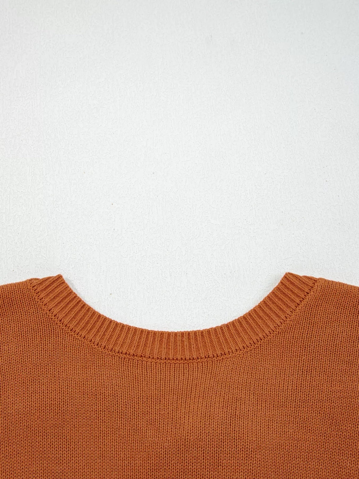 Warm rust solid-color sweater shown close up, featuring a soft knit texture, wide ribbed crew neckline, and cleanly finished shoulder seams.