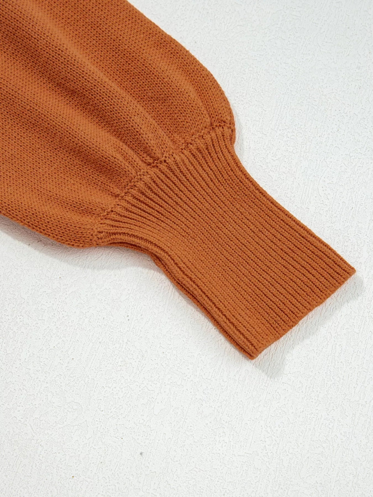 Solid rust-orange ribbed knit sweater sleeve with a wide ribbed cuff, visible seam construction, and a soft slightly stretchy texture.